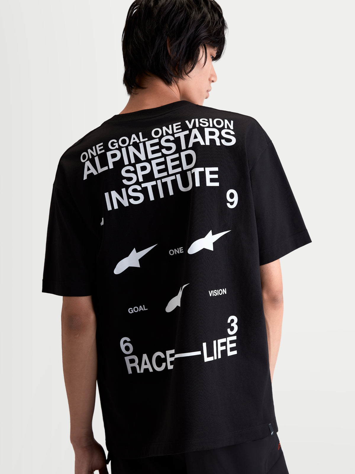 Alpinestars T-Shirt Institute Oversized CSF, t-shirt de sportswear à manches courtes, noir et blanc, mélange coton et polyester, vue de dos sur un modèle montrant les graphiques Alpinestars Speed Institute et Race-Life, coupe oversized décontractée.