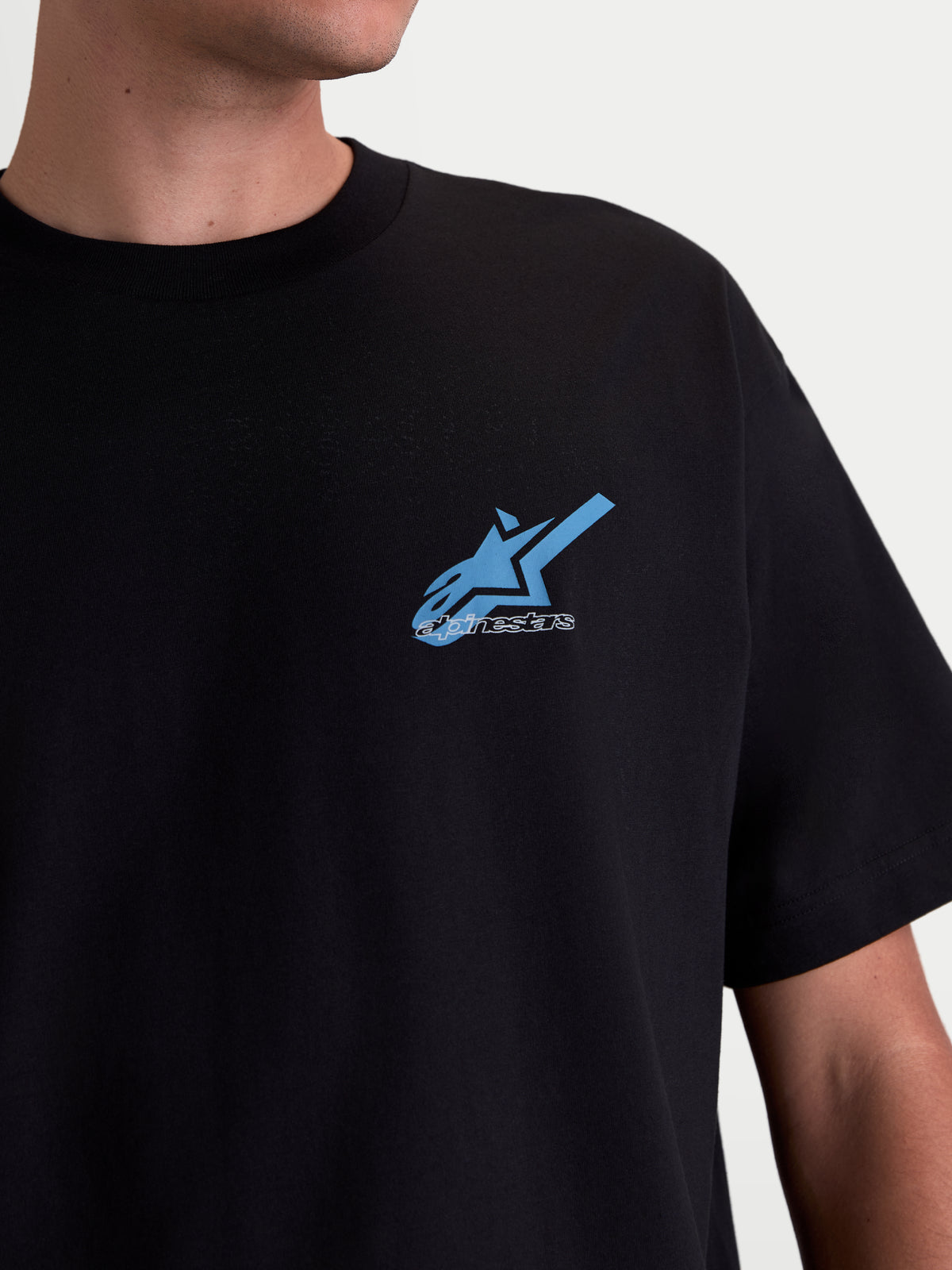 Alpinestars Ghost Oversized CSF, t-shirt à manches courtes de style sportswear, noir avec logo Astars bleu et blanc imprimé sur la poitrine, gros plan sur un modèle.