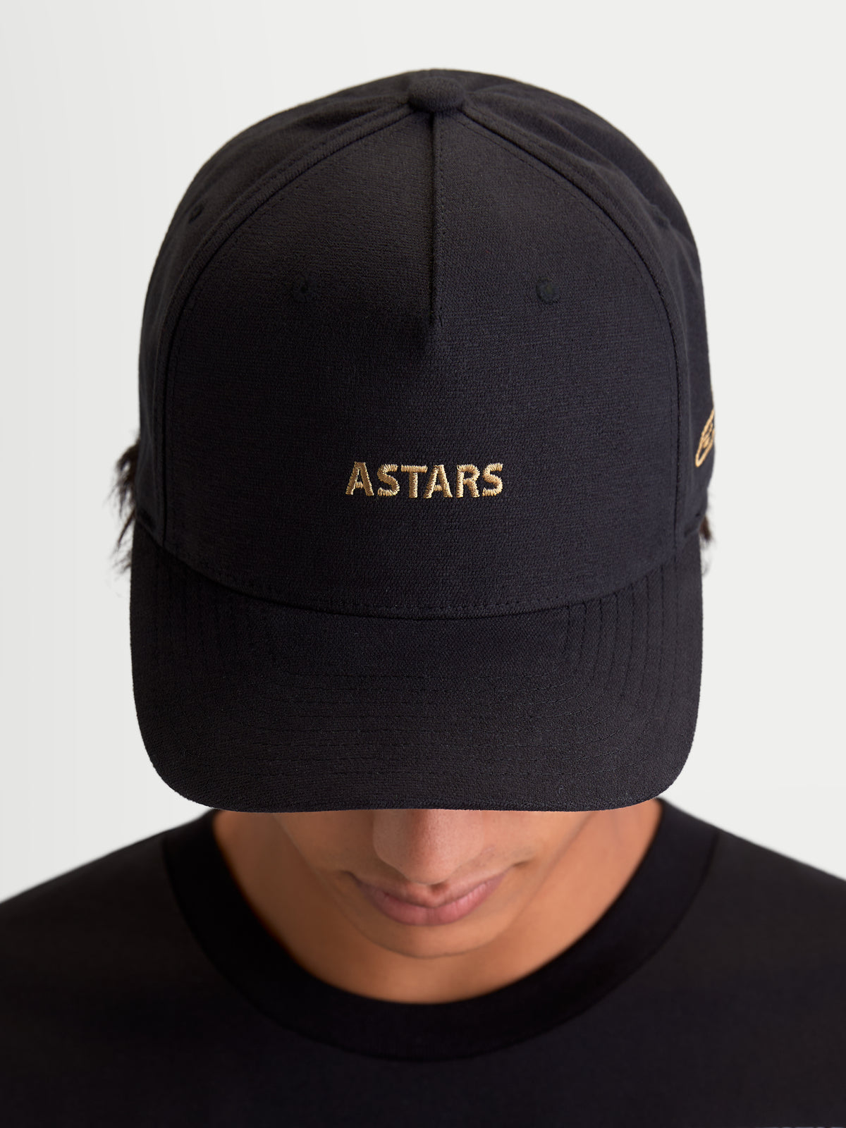 Alpinestars Casquette County Canvas, casquette de sportswear noire avec logo ASTARS doré brodé, visière incurvée et couronne structurée, tissu oxford, vue de face sur un modèle, style inspiré du sport automobile.