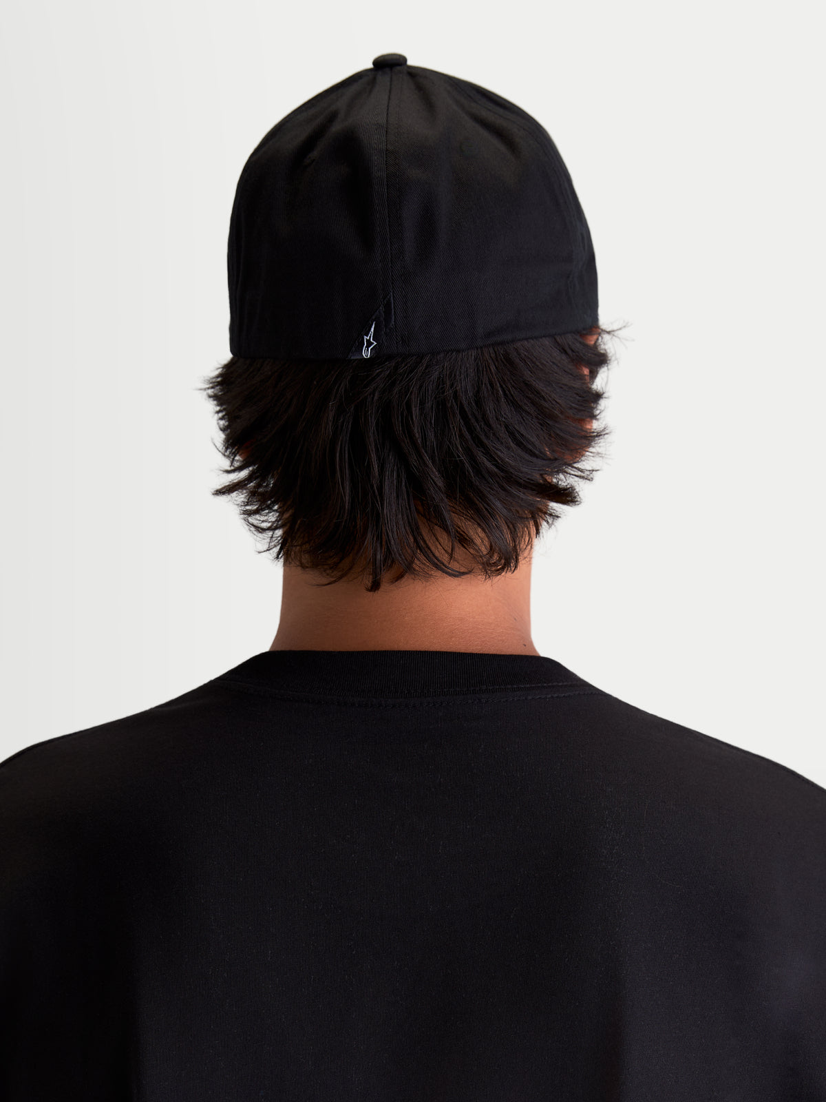 Alpinestars Arclight, casquette sportswear noire, vue de dos sur modèle avec un petit logo Astars blanc à l'arrière, couronne structurée et construction flex back en sergé de coton durable.