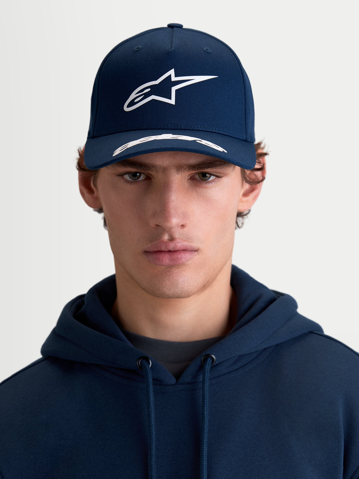Alpinestars Arclight, casquette de sportswear à visière incurvée, bleu marine et blanche, vue de face portée par un modèle, avec couronne structurée, logo Astars en relief texturé et sergé de coton premium
