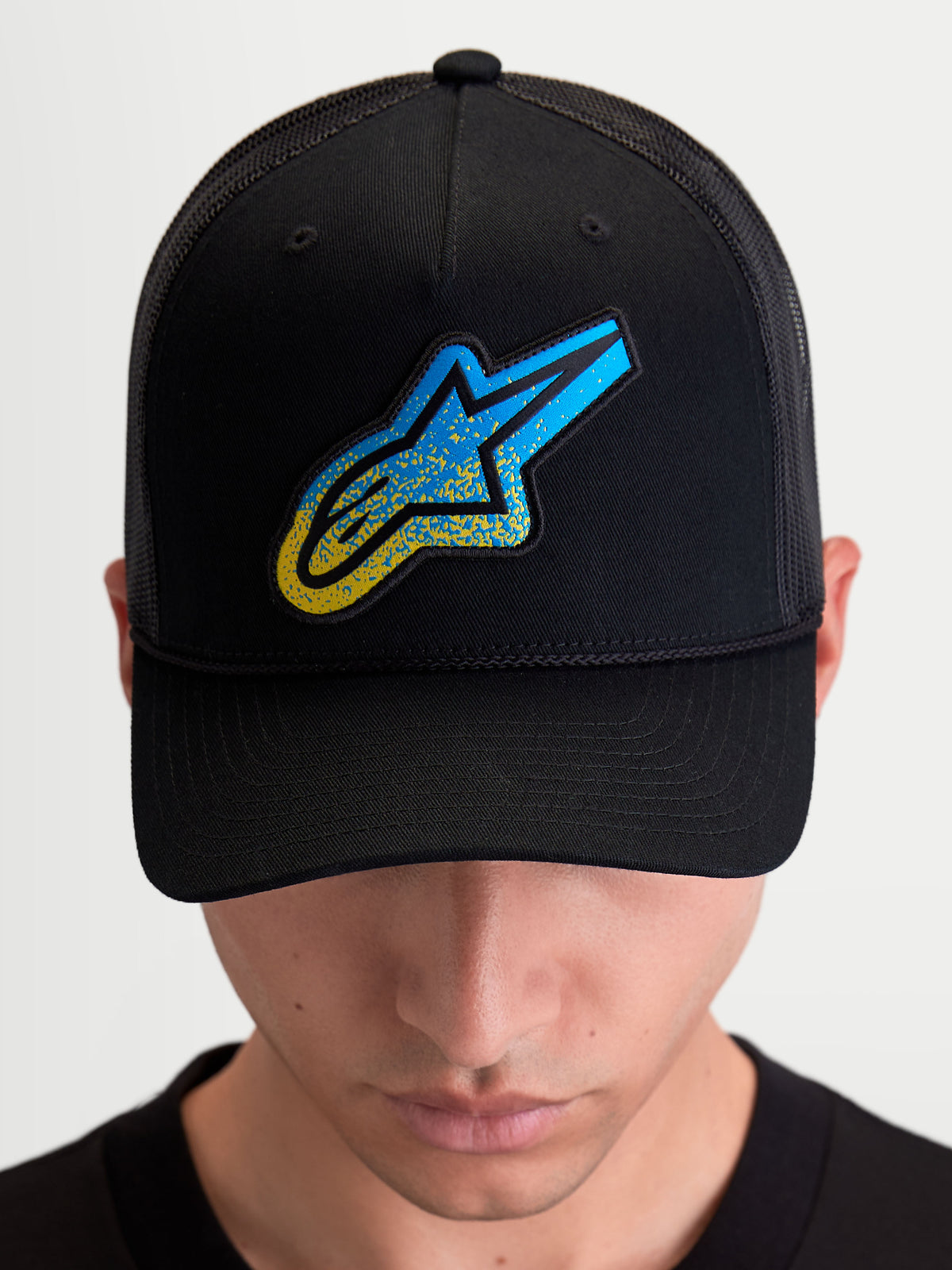 Alpinestars Casquette Trucker Meteorite, casquette de sportswear avec arrière en maille, noire et bleue, dotée d'un écusson logo Astars texturé, d'une couronne structurée et d'une visière incurvée, portée par un mannequin.
