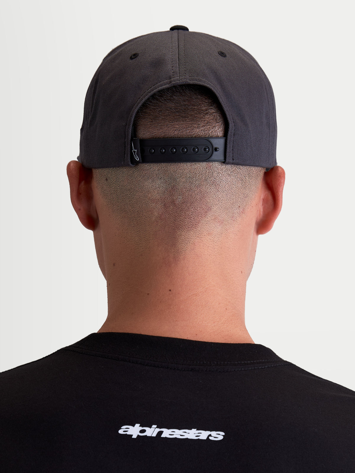 Alpinestars Stadium Snapback, casquette de sportswear grise et noire, vue arrière sur modèle montrant la fermeture snapback réglable et la couronne structurée, construction en sergé de coton durable