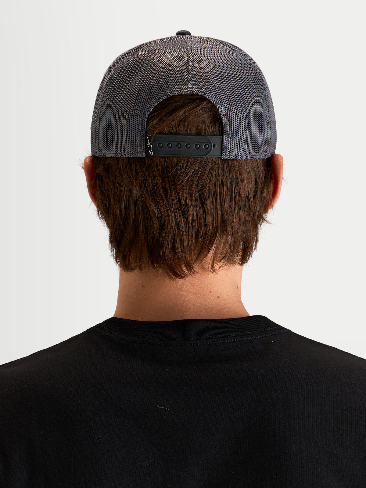 Alpinestars Casquette Trucker Ten, casquette sportswear gris foncé, vue de dos sur un modèle montrant la fermeture snapback ajustable, les panneaux arrière en mesh et le détail de l'étiquette au dos