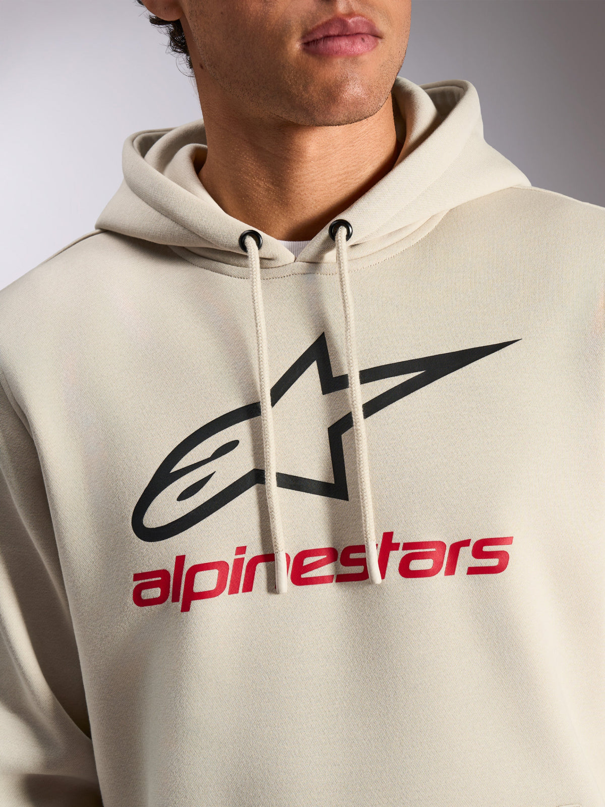 Sweat à capuche Alpinestars Always V3, style streetwear décontracté, blanc cassé avec logo étoile noir et texte Alpinestars rouge, capuche à cordon de serrage, polaire premium, design moderne inspiré des sports mécaniques