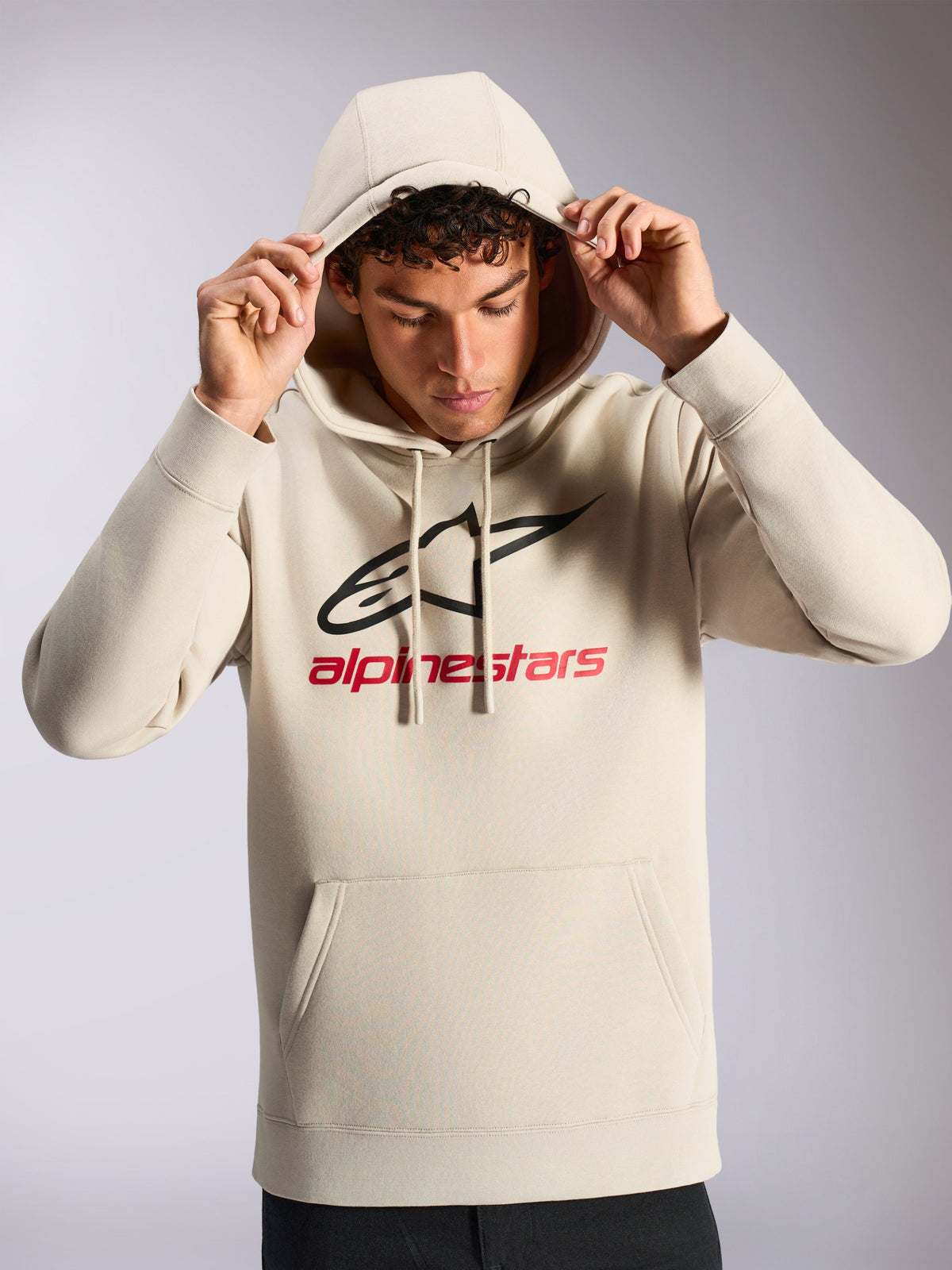 Alpinestars Always V3 Hoodie, modèle masculin portant un sweat à capuche en polaire blanc cassé, logo linéaire noir et rouge à l'avant, capuche avec cordon de serrage, poche kangourou, streetwear décontracté inspiré par le sport automobile