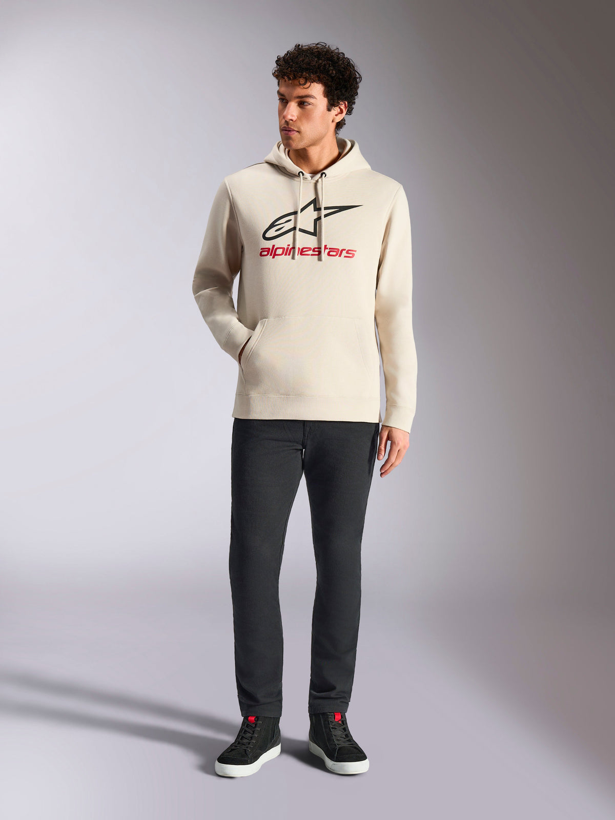 Alpinestars Always V3 Hoodie, streetwear décontracté, blanc cassé avec logo étoile noir et lettrage rouge, capuche à cordon de serrage, manches longues, porté par un mannequin homme avec pantalon noir et baskets noires