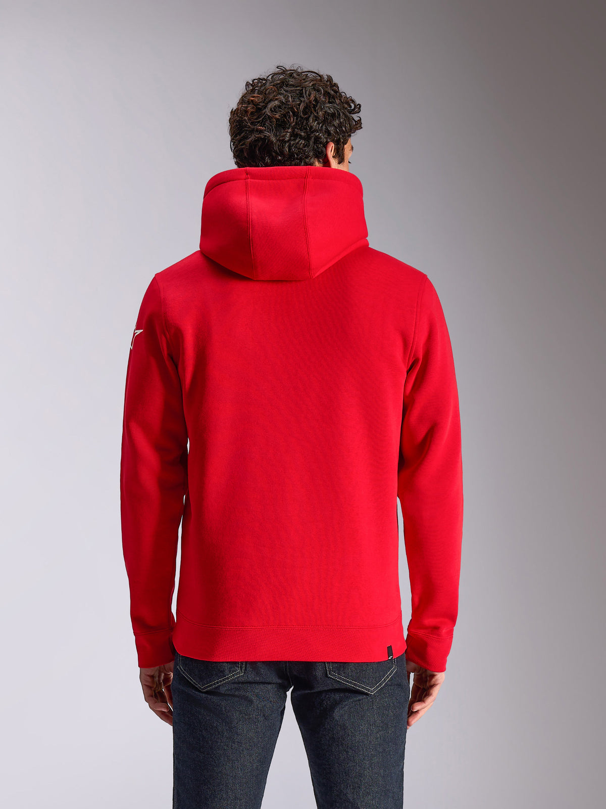 Alpinestars Linear Wordmark V3 Hoodie, vue arrière d'un sweat à capuche rouge, avec un logo Ageless blanc sur la manche, poignets et ourlet en côtes, vêtement streetwear décontracté inspiré du sport automobile