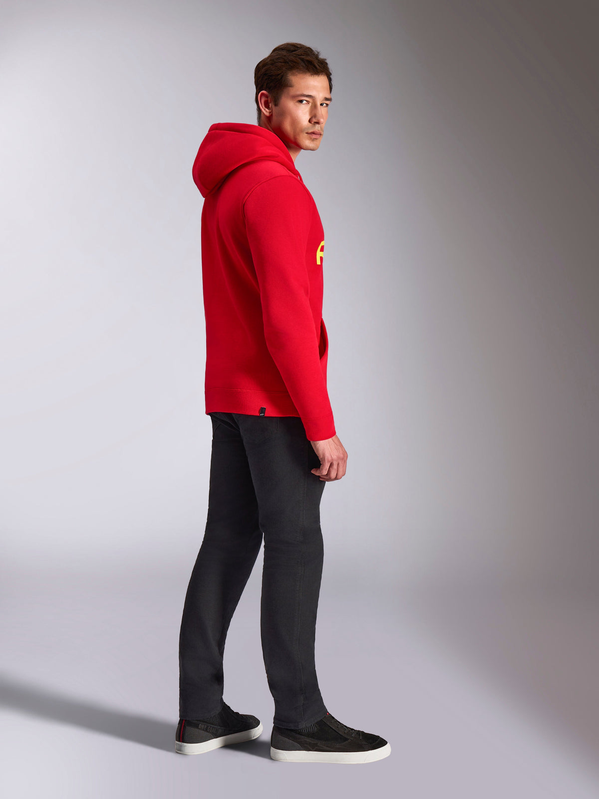Sweat à capuche Alpinestars Ride V3, vêtement sportswear décontracté, rouge avec marquage jaune haute visibilité, modèle masculin portant un sweat à capuche rouge avec un pantalon noir et des baskets, vue de profil, modèle en polaire à enfiler avec poignets et ourlet en côtes