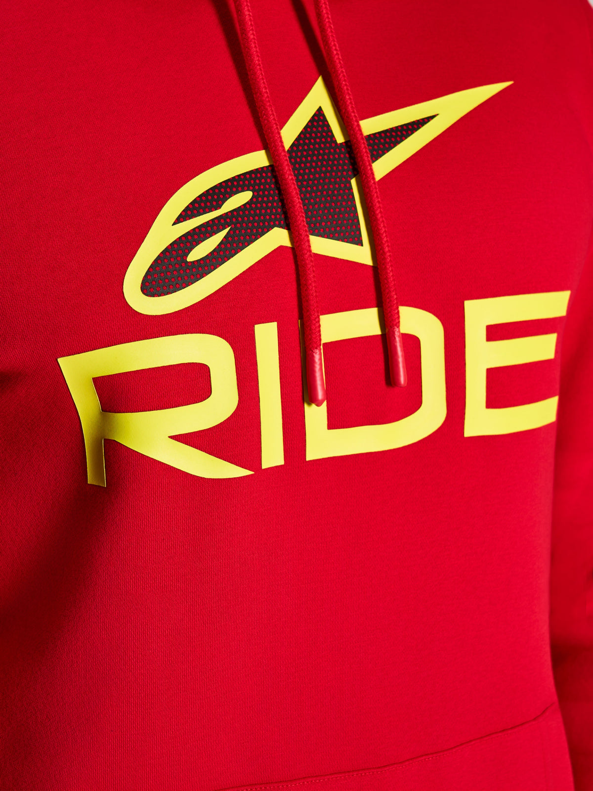 Sweat à capuche Alpinestars Ride V3, gros plan du graphisme sur la poitrine, rouge avec texte RIDE jaune haute visibilité et logo étoile noir perforé, cordons de serrage rouges avec embouts trempés, polaire premium style streetwear