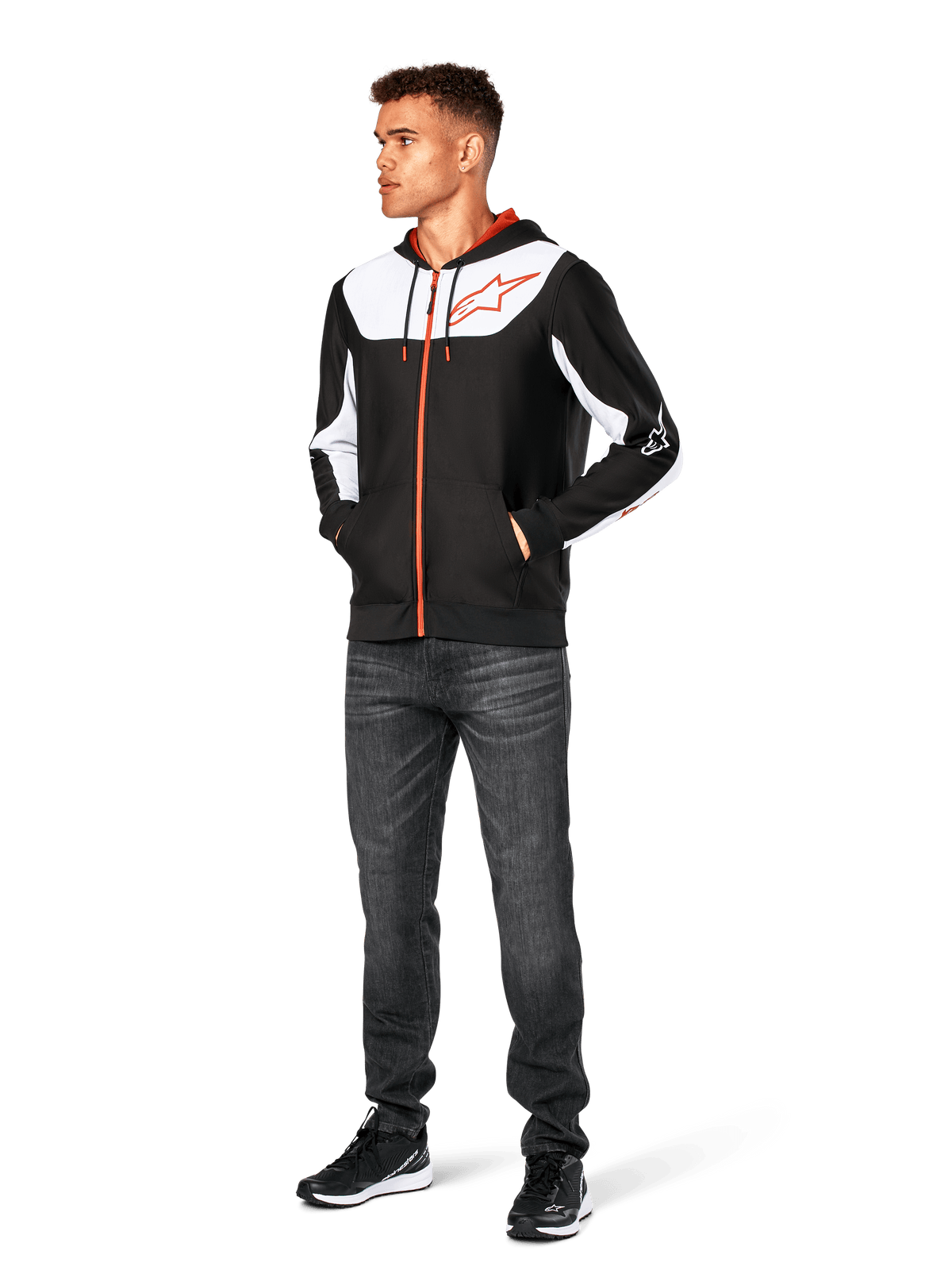 Sweat à capuche Alpinestars Sessions V3, sweat à capuche zippé décontracté, noir, blanc et rouge, porté par un mannequin avec un jean foncé et des baskets noires, doté d'empiècements blancs sur la poitrine et les manches, détails de fermeture éclair et cordons de serrage rouges, grand logo sur la poitrine, polaire en polyester au style streetwear inspiré du sport automobile
