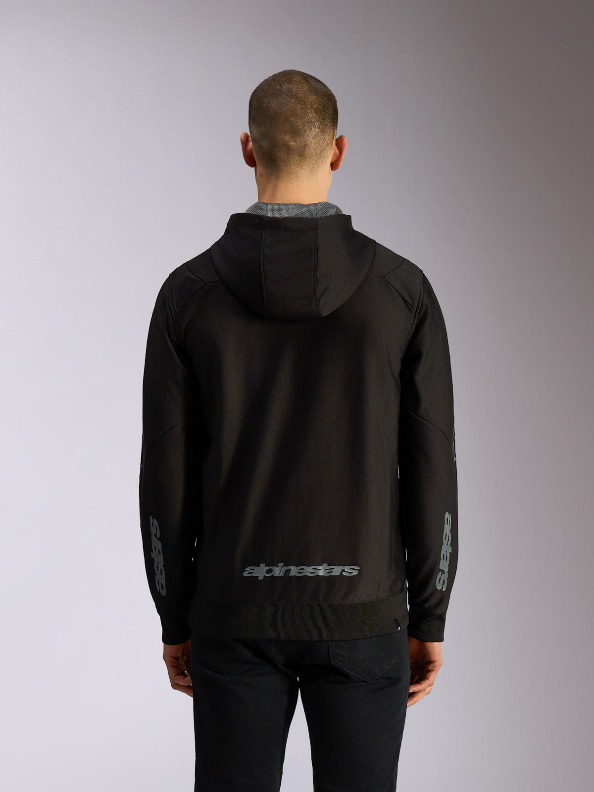 Sweat à capuche Alpinestars Sessions V3, vue de dos, sweat zippé noir avec lettrage Alpinestars gris en bas du dos, marquage Astars sur les manches, poignets et ourlet côtelés, style streetwear motorsport décontracté
