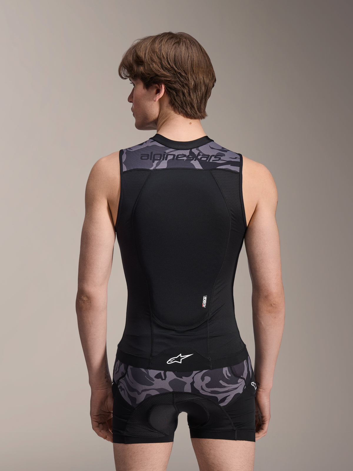Gilet de protection Alpinestars A-Motion Plasma, Black Camo, vue de dos sur modèle masculin, construction en maille respirante avec protection dorsale Nucleon Plasma intégrée, accents camouflage gris sur les épaules et la taille, et logo Alpinestars.