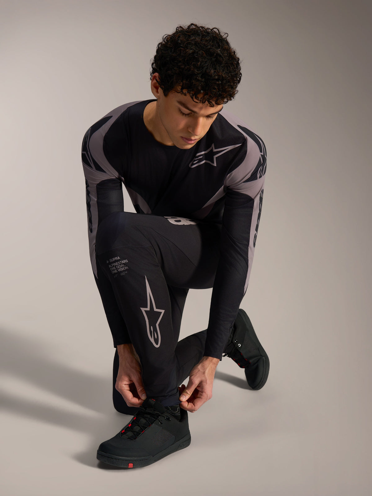 Pantalon A-Supra Elite Alpinestars noir, logos gris, porté par un mannequin à genoux pour le VTT de performance.