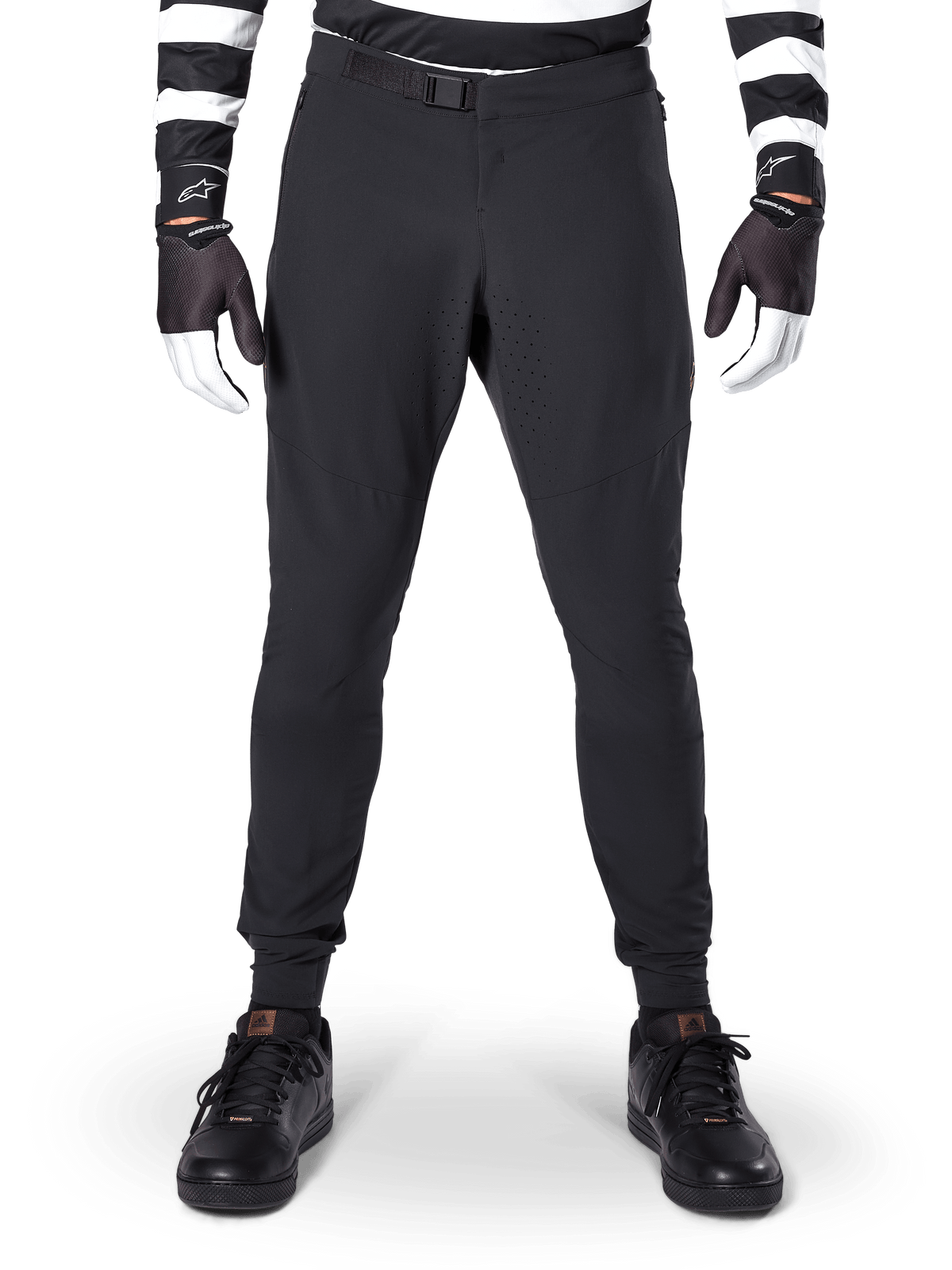 Pantalon Alpinestars A-Aria Elite, pantalon de VTT, noir, vue de face montrant les perforations laser et la fermeture à boucle magnétique, porté avec un maillot rayé noir et blanc et des gants noirs, équipement de cyclisme performant pour le trail