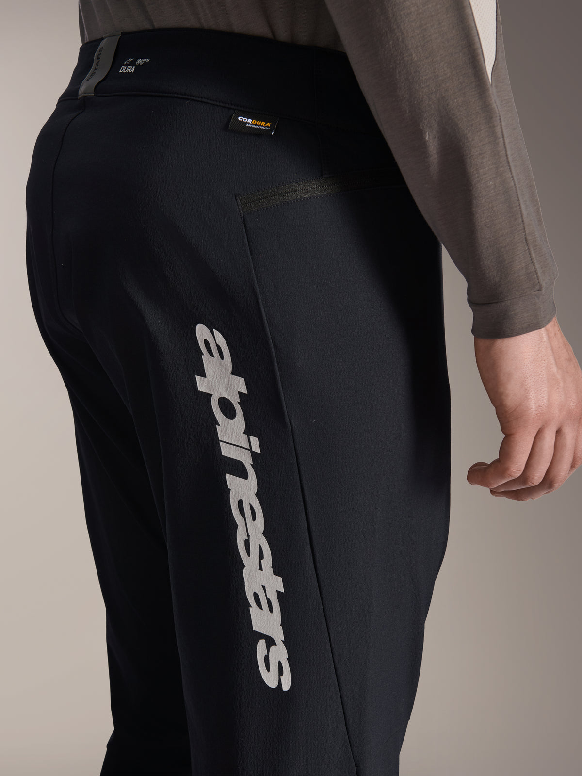 Alpinestars A-Dura Elite Pants, pantalon de VTT noir, vue de côté présentant un grand logo Alpinestars vertical sur la jambe, étiquette en tissu Cordura et poche latérale zippée, vêtement technique de cyclisme pour la pratique du tout-terrain