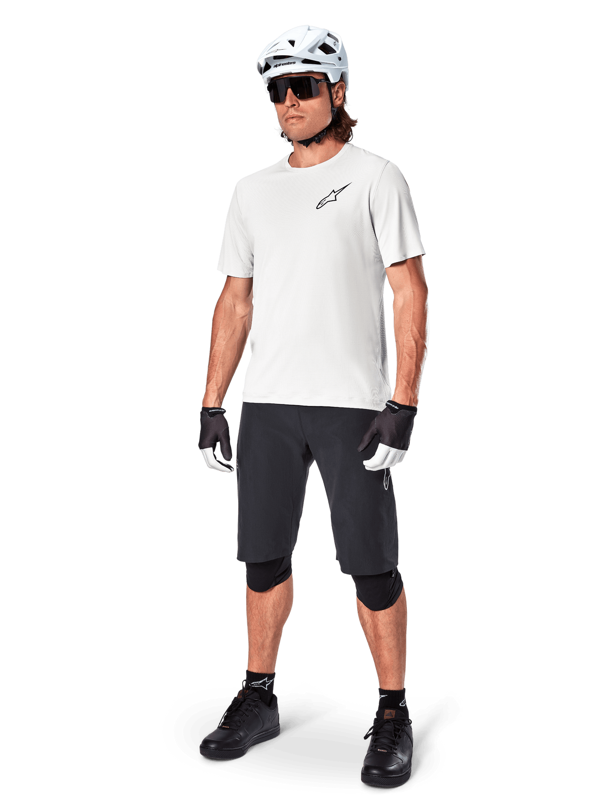 Vététiste homme portant le short Alpinestars A-Aria, short de cyclisme noir, associé à un maillot blanc à manches courtes, un casque de VTT blanc et un équipement technique noir, tenue complète pour la pratique du VTT tout-terrain