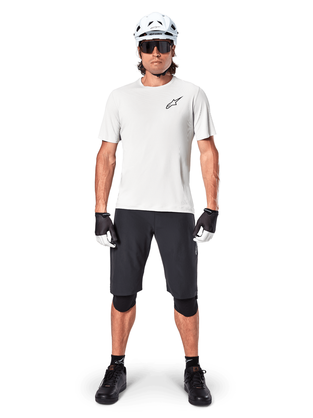 Vététiste homme portant le short Alpinestars A-Aria Noir, associé à un maillot technique blanc, un casque blanc et des protège-genoux noirs, équipement de cyclisme tout-terrain professionnel, vue de face complète