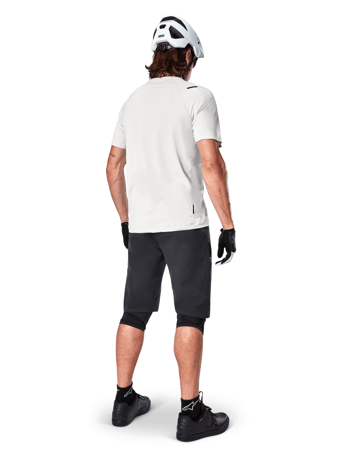 Vététiste de dos portant le short Alpinestars A-Aria noir, maillot de performance blanc à manches courtes, casque blanc, gants noirs et chaussures de VTT noires, équipement de cyclisme pour le trail
