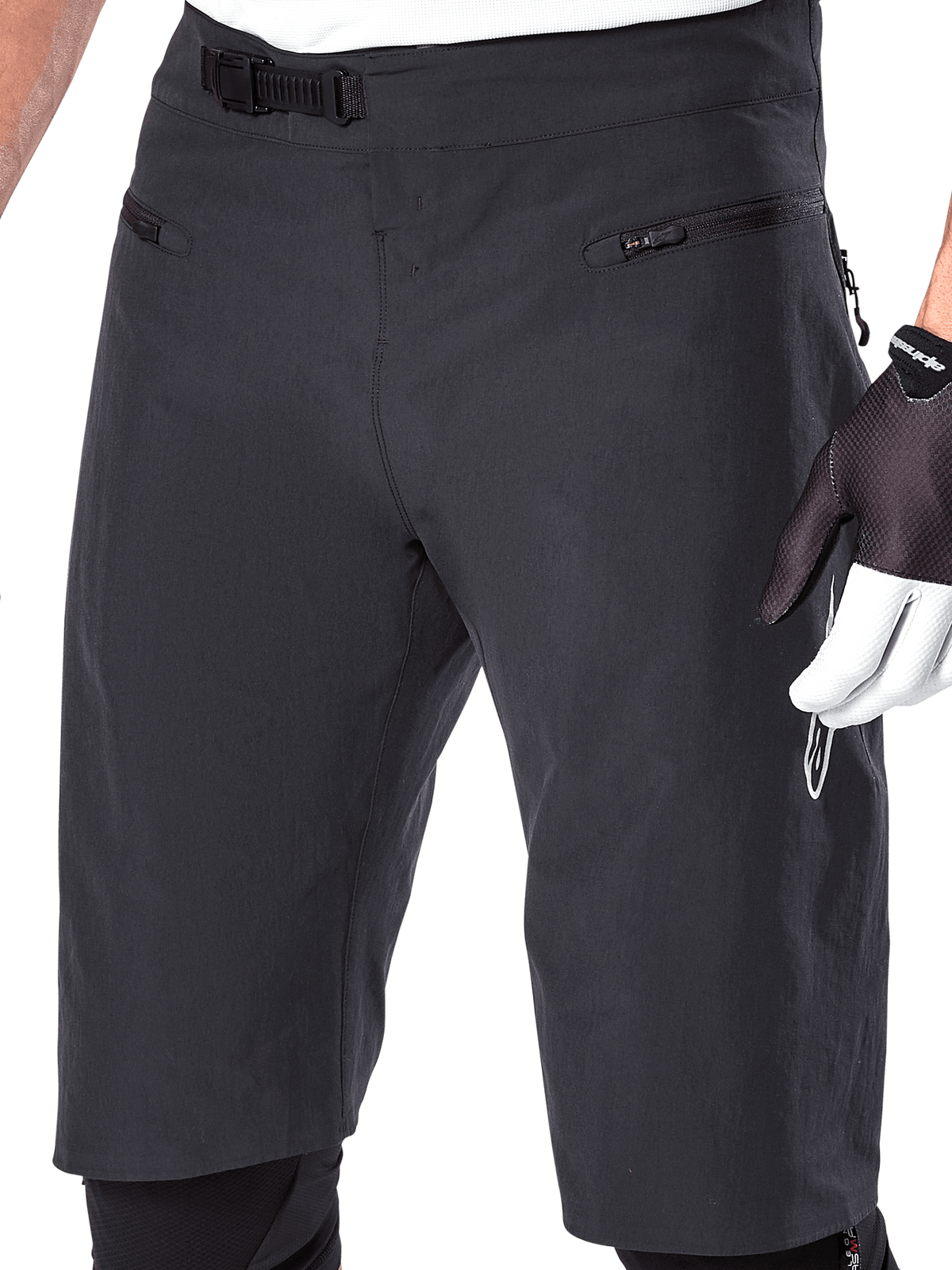 Short Alpinestars A-Aria, short de VTT, noir, vue rapprochée de la taille et des cuisses montrant le système de fermeture à rochet et les poches zippées, porté avec des gants de cyclisme noirs et blancs, équipement de performance pour le trail