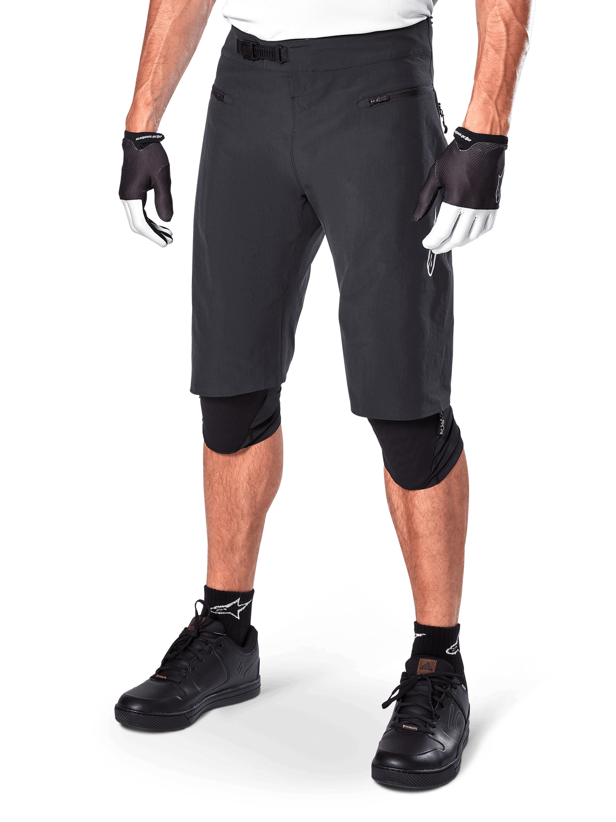 Alpinestars A-Aria Shorts, short de VTT noir, longueur genou avec poches avant zippées et boucle de taille à cliquet réglable, porté avec des genouillères noires, des chaussettes et des gants de cyclisme