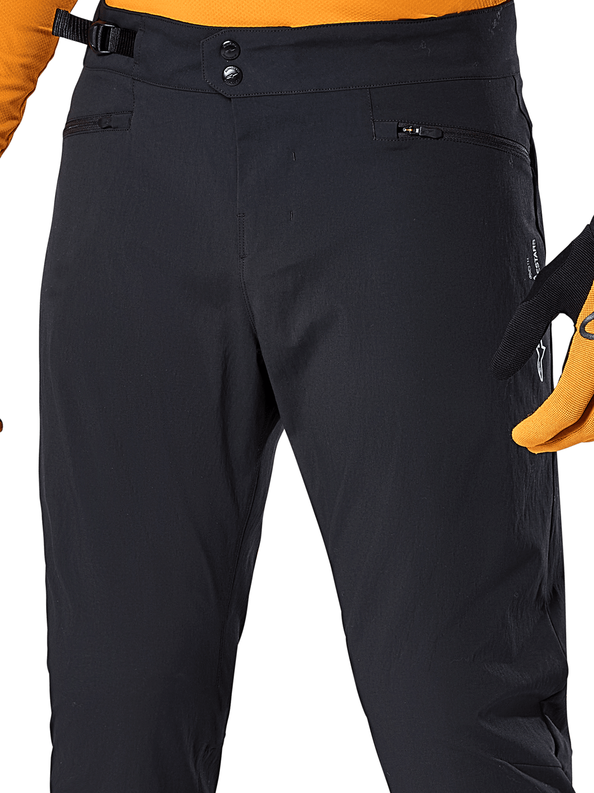 Alpinestars A-Dura Pants, Black MTB cycling pants, close-up view featuring double snap waist closure, adjustable side cinch, and zippered pockets, paired with an orange jersey and gloves