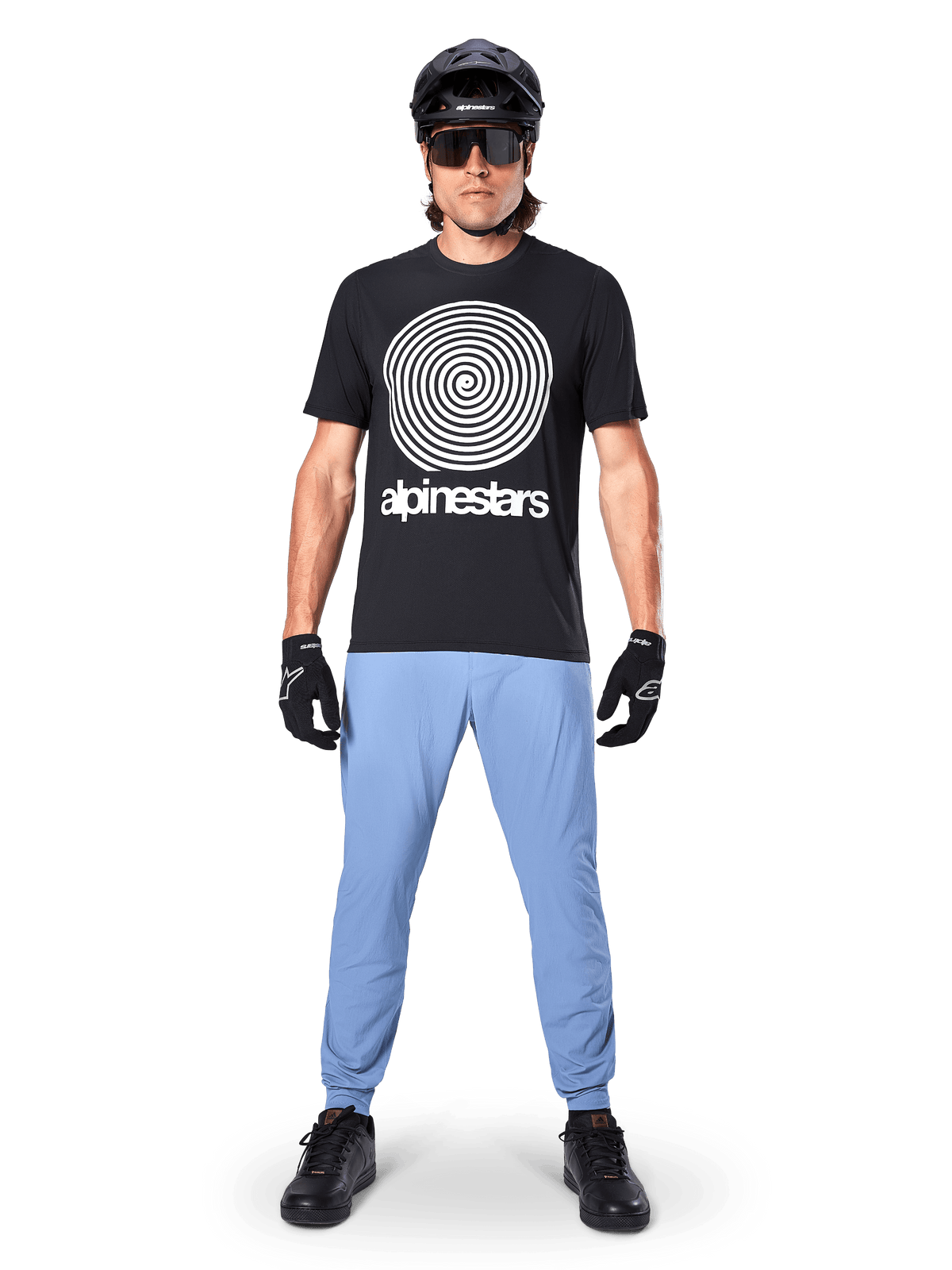 Pantalon Alpinestars A-Dura, Bleu Infinity, pantalon de VTT porté avec un t-shirt noir à motif spirale, des gants noirs et un casque noir, doté d'un tissu extensible durable et de chevilles élastiquées, équipement de VTT haute performance