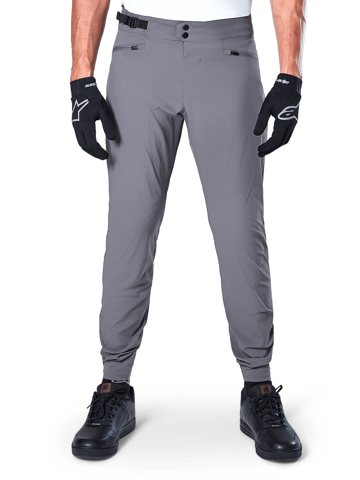 Pantalon Alpinestars A-Dura, pantalon de VTT gris foncé, vue de face porté avec des gants noirs et des baskets noires, doté d'une double fermeture à pression à la taille, de poches mains zippées et de chevilles élastiquées, vêtement de cyclisme durable pour le trail