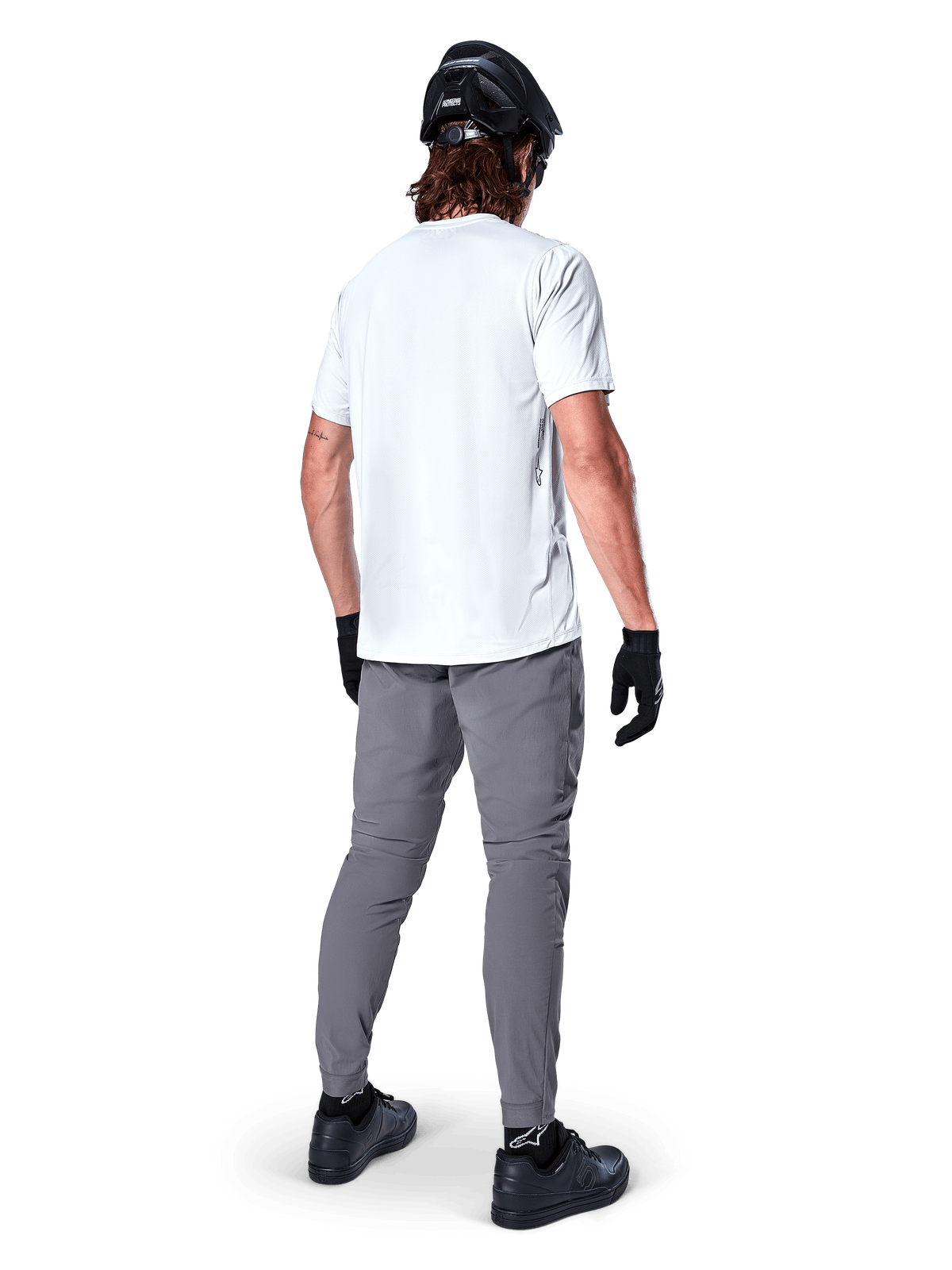 Pantalon Alpinestars A-Dura, pantalon de VTT gris foncé vu de dos, porté avec un t-shirt blanc à manches courtes, un casque de VTT noir, des gants et des chaussures noirs, coupe régulière avec chevilles élastiquées, équipement de cyclisme tout-terrain durable