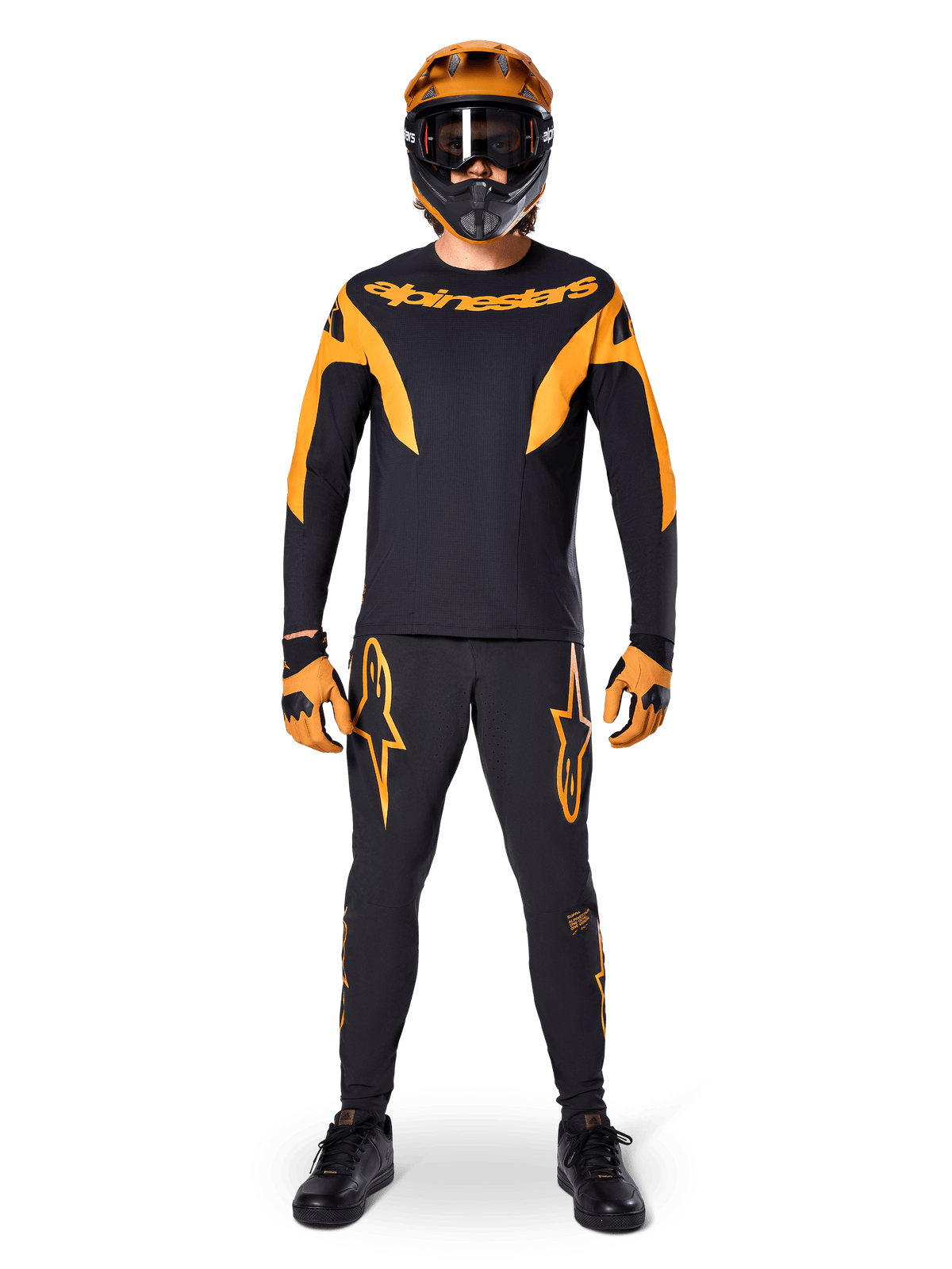 Alpinestars A-Supra Race Pants, pantalon de course VTT, noir et orange, porté par un pilote avec une tenue complète comprenant un maillot noir et orange, un casque orange et des gants assortis, avec logos étoiles orange sur les jambes