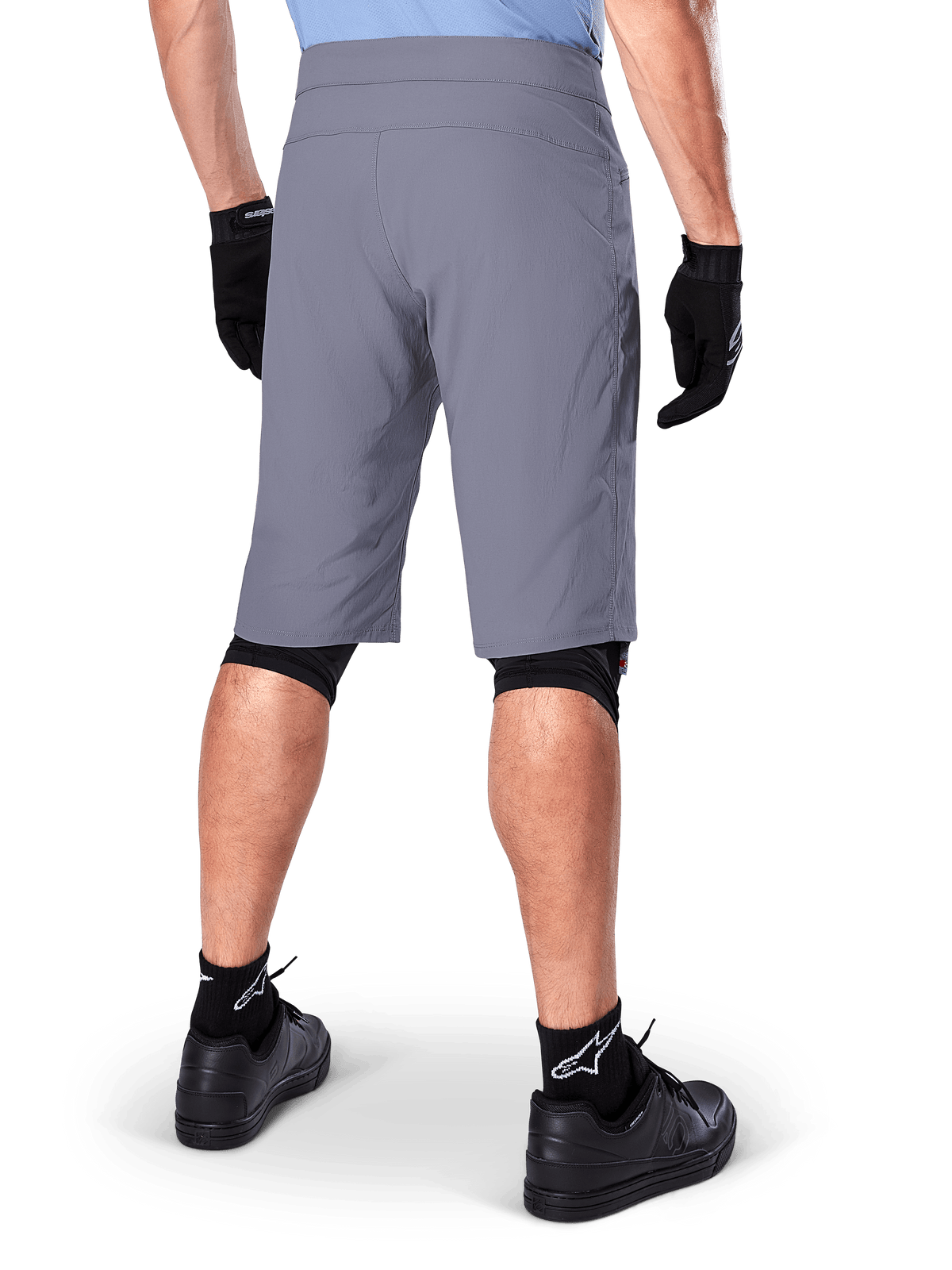 Short Alpinestars A-Dura, short de VTT gris foncé, vue arrière portée par un cycliste avec gants noirs, genouillères noires et chaussettes noires à logo Alpinestars, construction durable pour le cyclisme tout-terrain