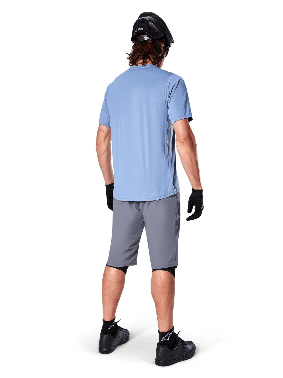 Alpinestars A-Dura Shorts, Dark Gray MTB Shorts, rear view, worn with a light blue short-sleeve jersey and black mountain bike helmet, black gloves and socks with black shoes, functional and durable gear for off-road cycling