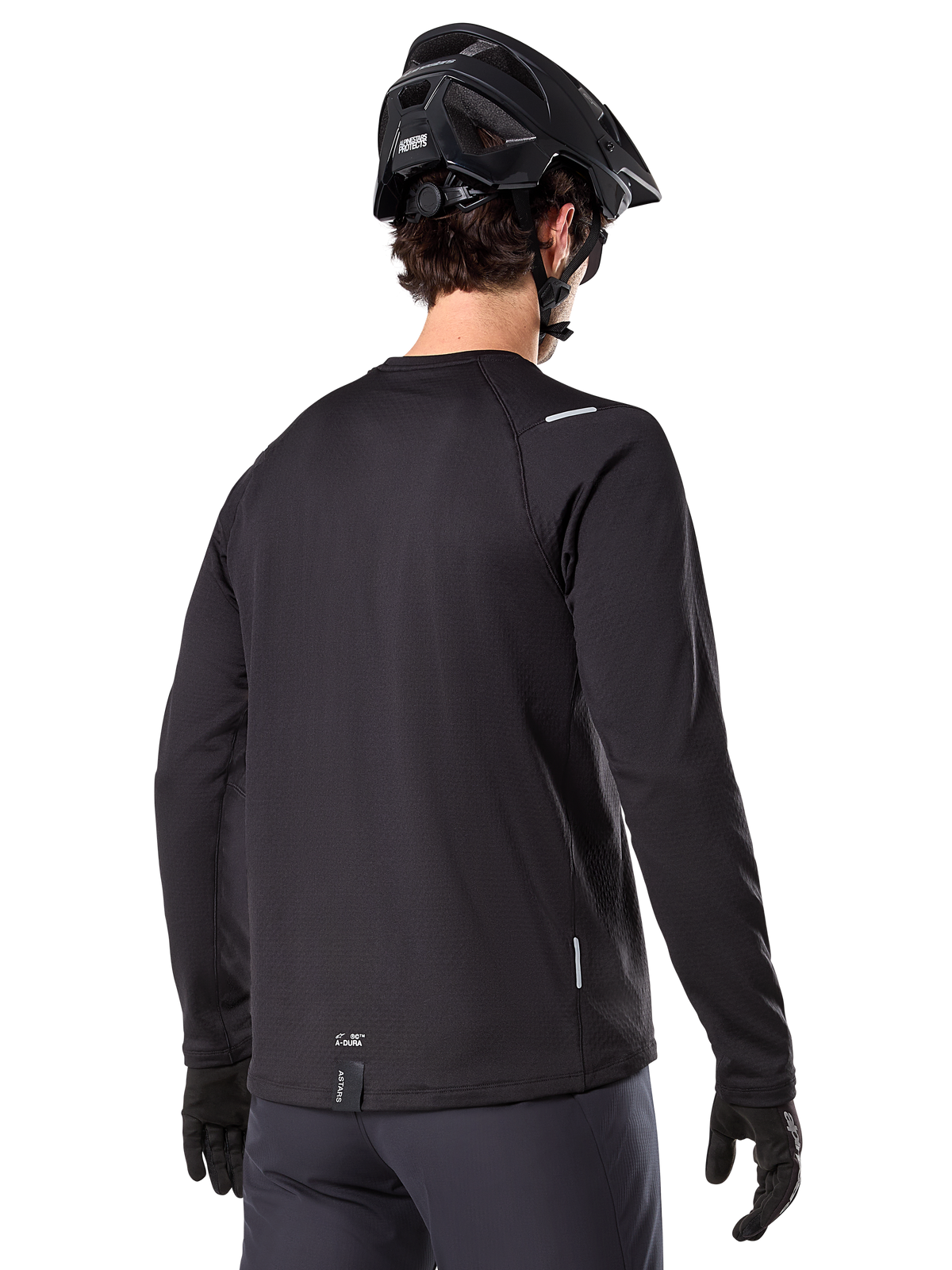 Maillot thermique Alpinestars A-Dura, maillot de VTT à manches longues, noir, vue de dos montrant la queue allongée, de petits détails réfléchissants et le marquage sur l'ourlet, porté avec un casque noir et des gants pour le cyclisme par temps froid