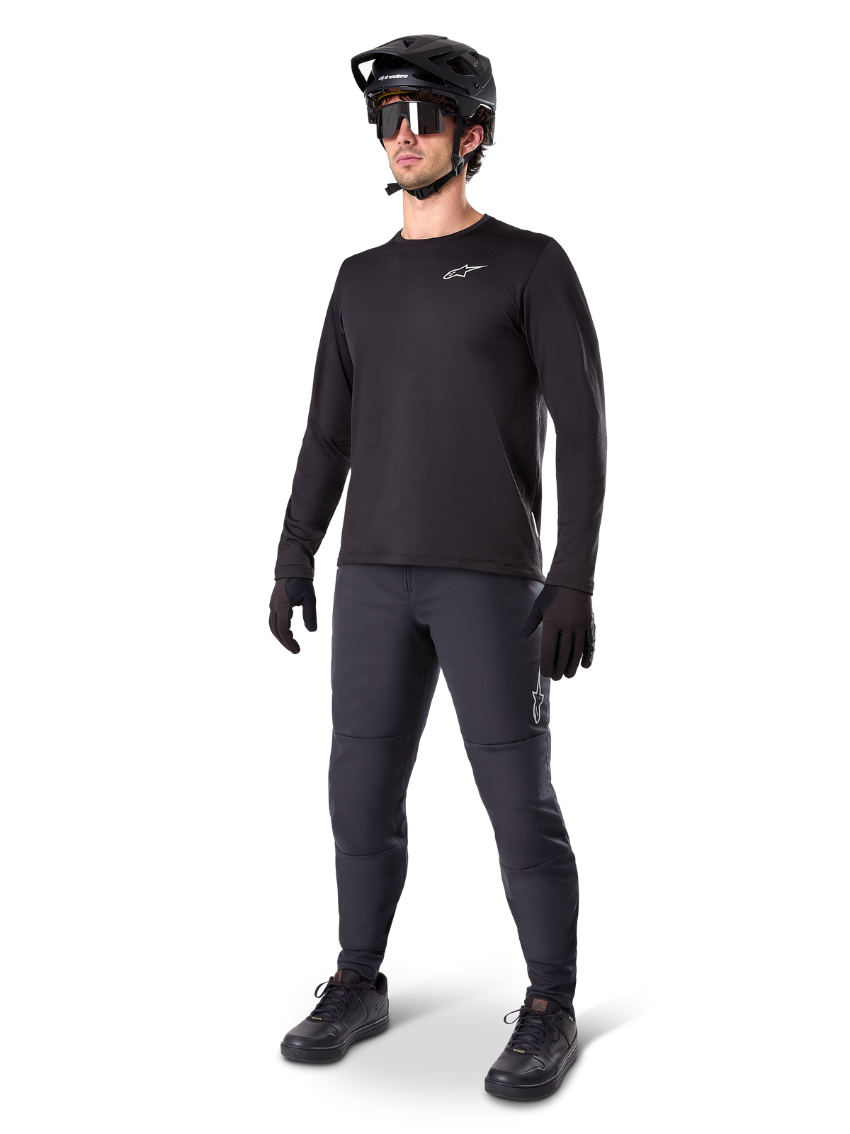 Modèle portant le maillot thermique Alpinestars A-Dura, maillot de VTT noir à manches longues, casque de VTT noir, lunettes de soleil et pantalon gris foncé, avec un petit logo blanc sur la poitrine, conception en polaire isolante pour rouler par temps froid