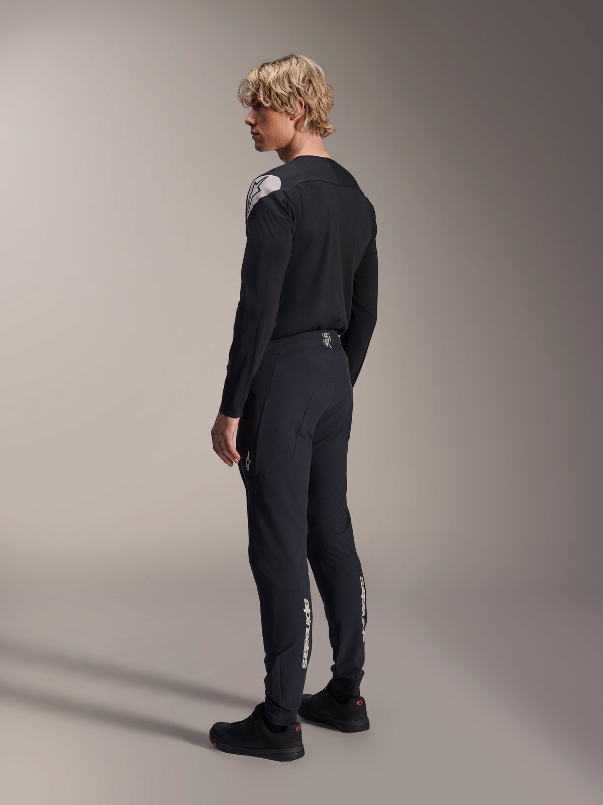 Maillot à manches longues Alpinestars A-Aria Polartec Elite, noir, porté par un mannequin de profil arrière, arborant un logo blanc sur l'épaule, associé à un pantalon de cyclisme noir assorti, tenue de VTT professionnelle