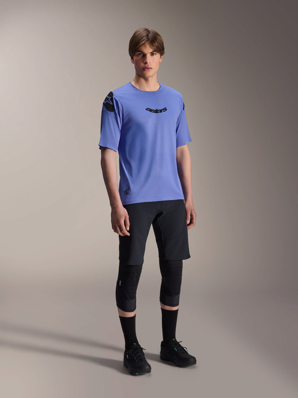 Mannequin homme portant le maillot à manches courtes Alpinestars A-Aria Polartec Elite en Baja Blue, associé à un short de VTT noir et des genouillères, avec des logos Astars noirs sur la poitrine et l'épaule, équipement de VTT haute performance
