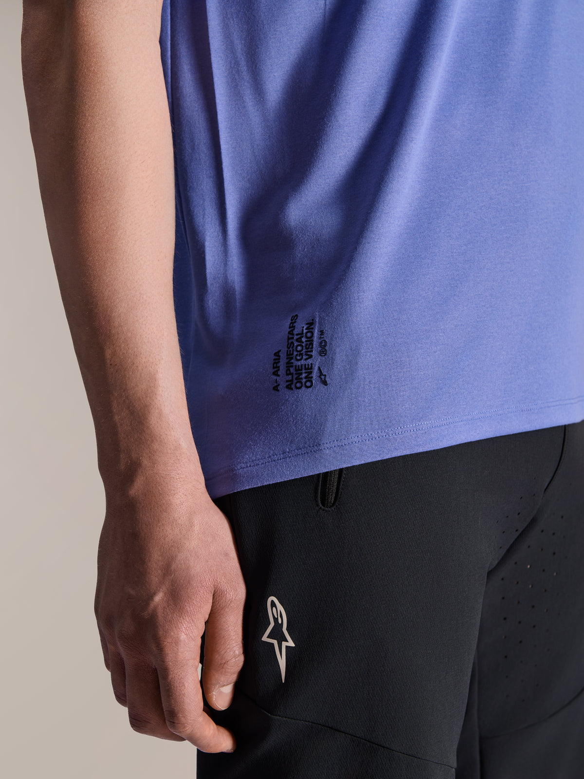 Maillot à manches courtes Alpinestars A-Aria Polartec Elite en Baja Blue, détail de l'ourlet latéral inférieur avec l'inscription noire 'One Goal. One Vision.' et le logo ASTARS, associé à un short de VTT noir.