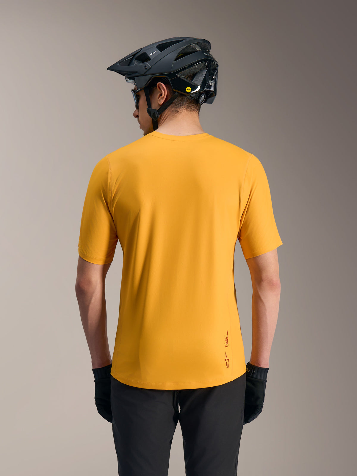 Maillot A-Dura Ride orange à manches courtes, haut de VTT léger avec logo et ourlet arrière allongé, vu de dos avec casque.