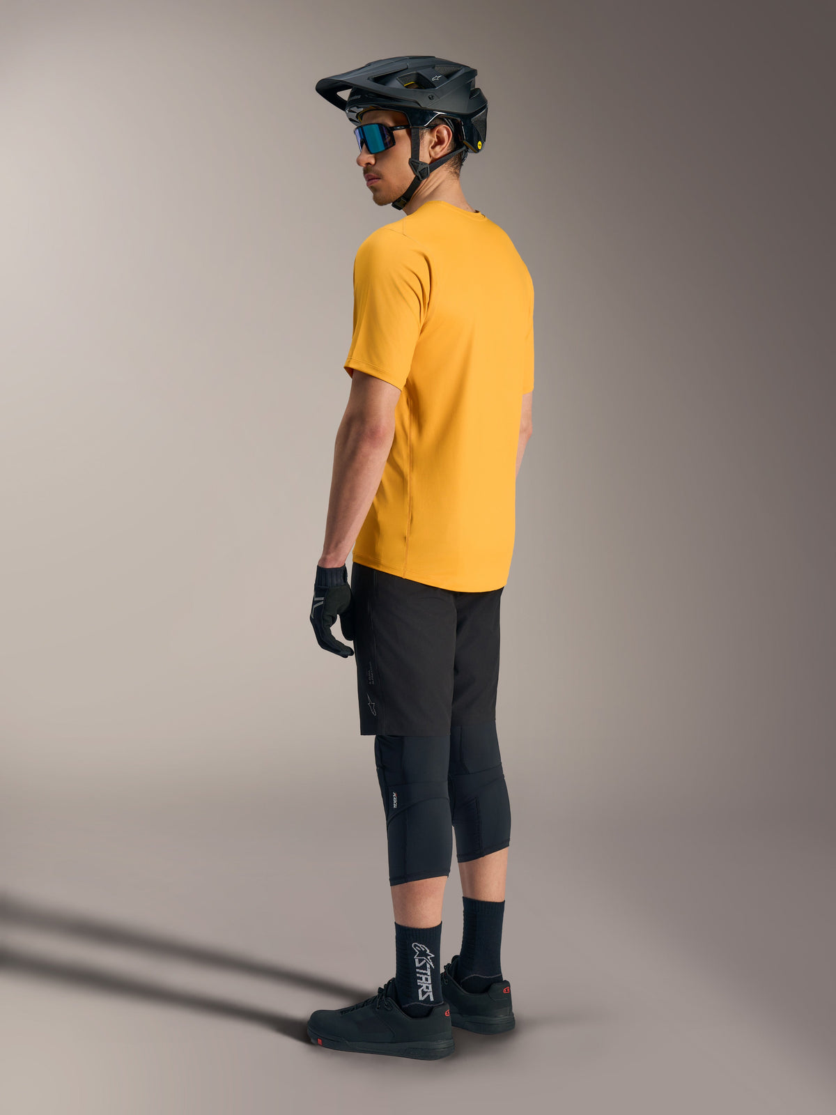 Maillot orange Alpinestars A-Dura Ride à manches courtes, vu de dos sur un pilote VTT avec casque et tenue noirs.