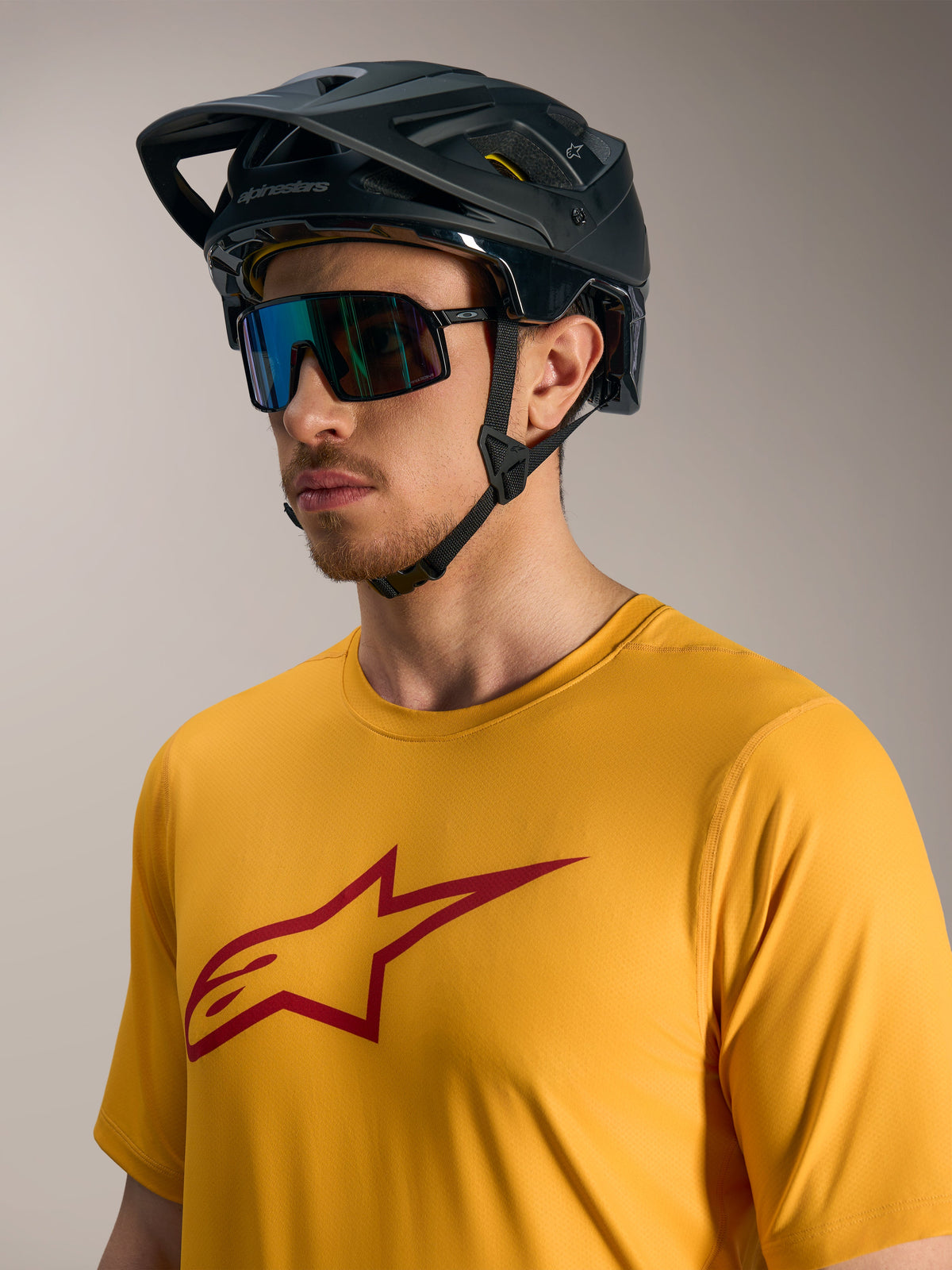 Maillot Alpinestars A-Dura Ride orange avec logo Astars rouge, casque VTT noir et lunettes de performance.