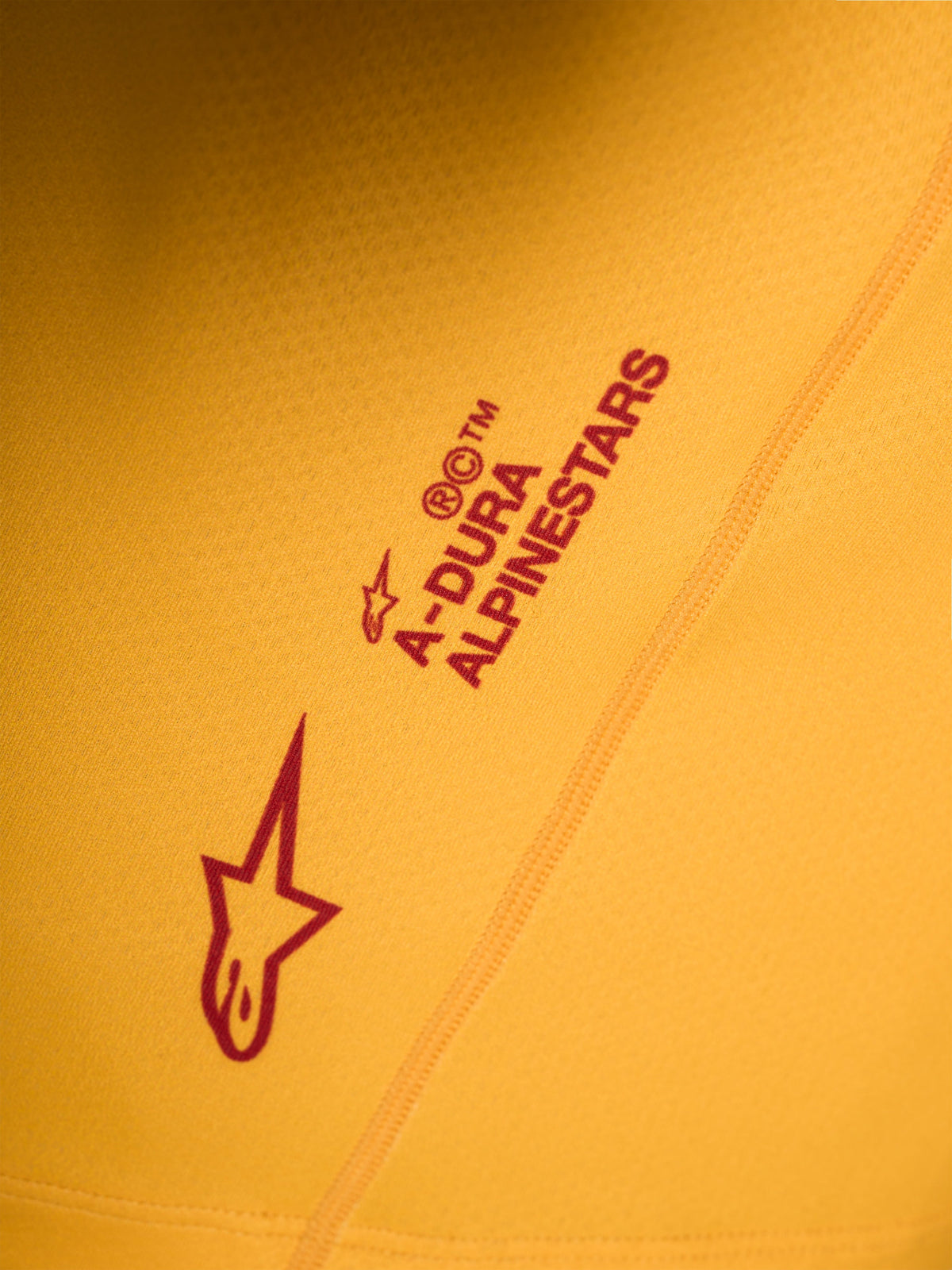 Détail du maillot A-Dura Ride orange, logos Astars et Alpinestars rouges sérigraphiés sur tissu extensible.