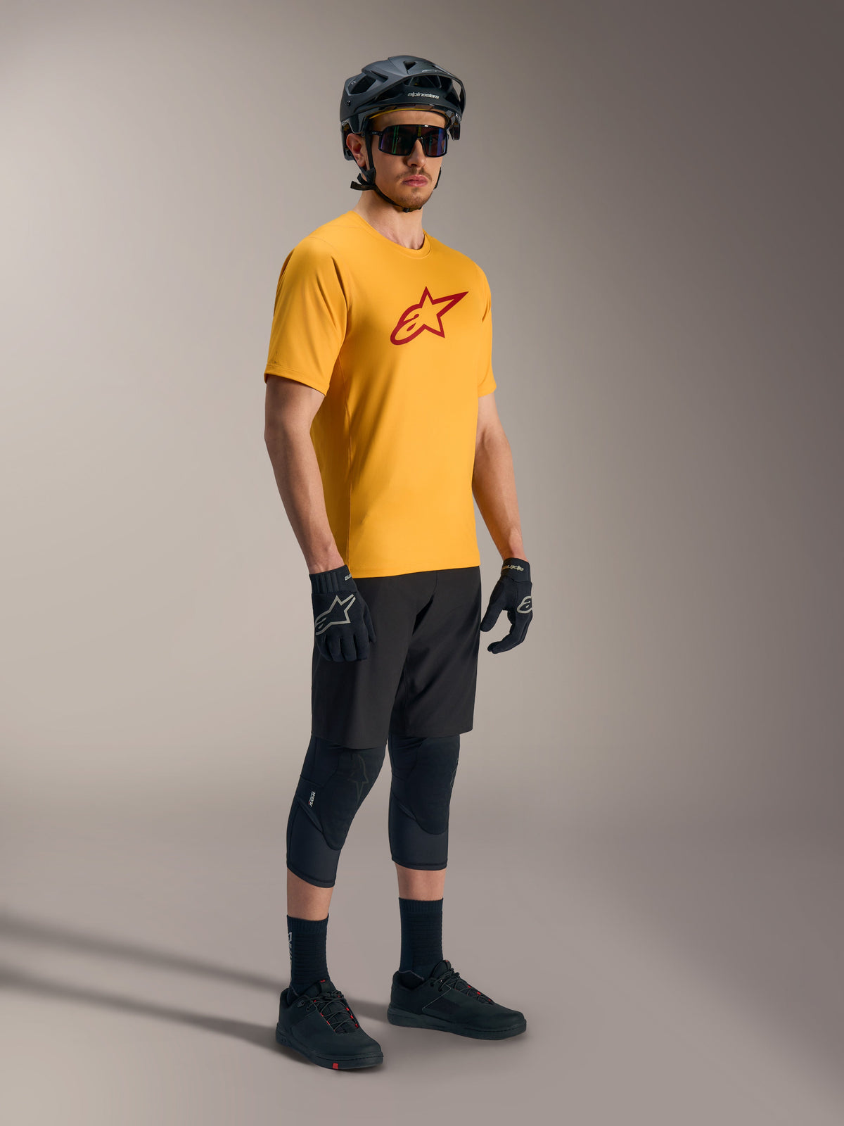 Maillot A-Dura Ride orange à manches courtes avec logo Astars rouge, associé à un équipement de VTT et un casque noirs.