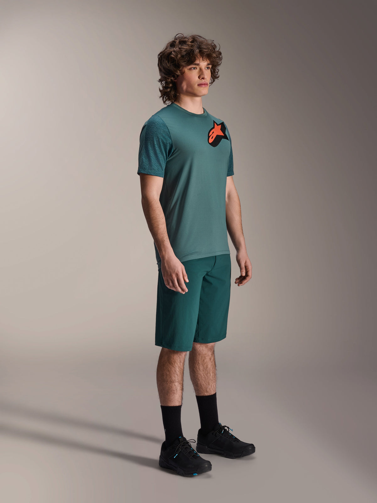 Alpinestars A-Dura Lipan Jersey, Short Sleeve MTB Jersey, Silver Pine Green, featuring an orange and black Astars logo on the chest, worn with matching green shorts and black cycling shoes, casual trail style