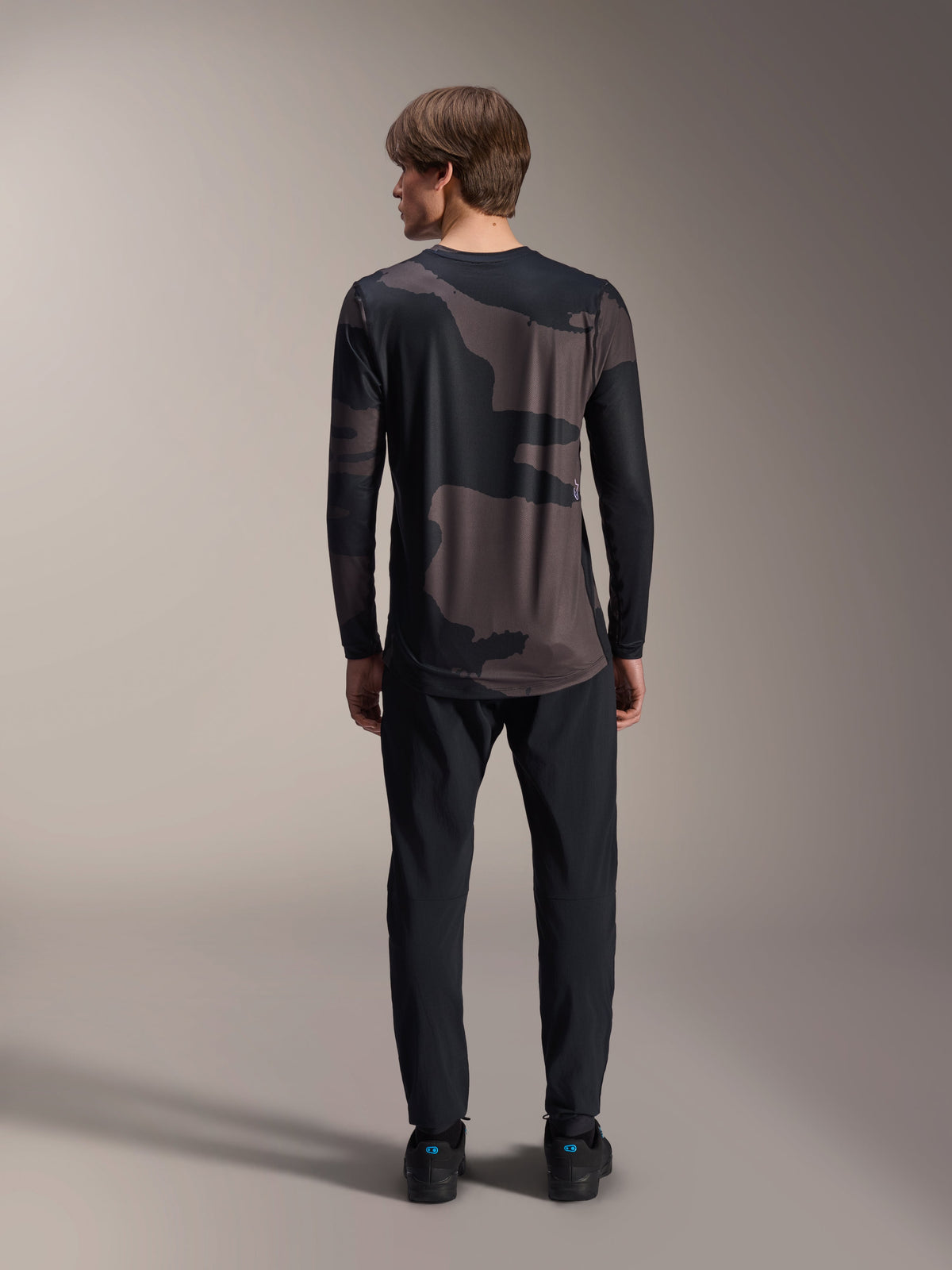 Maillot à manches longues Alpinestars A-Dura Hollow Camo, Camo noir, vue de dos porté avec un pantalon noir, présentant un motif camouflage sombre et un pan arrière allongé pour une couverture optimale en VTT.