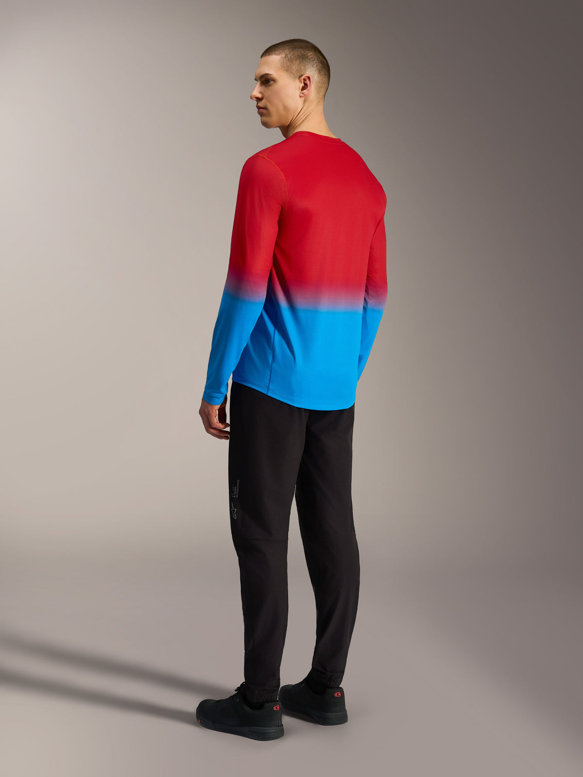 Maillot VTT Alpinestars A-Dura ASTARS 2.0, dégradé rouge et bleu, vue de dos sur modèle en pantalon noir.