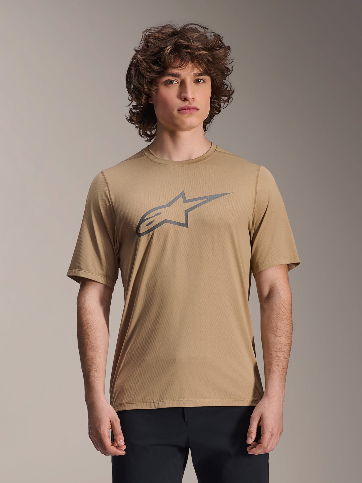 Maillot à manches courtes Alpinestars A-Dura Astar, marron clair, porté par un mannequin homme avec un pantalon noir, logo étoile Alpinestars gris sur la poitrine, maillot de VTT décontracté pour le trail