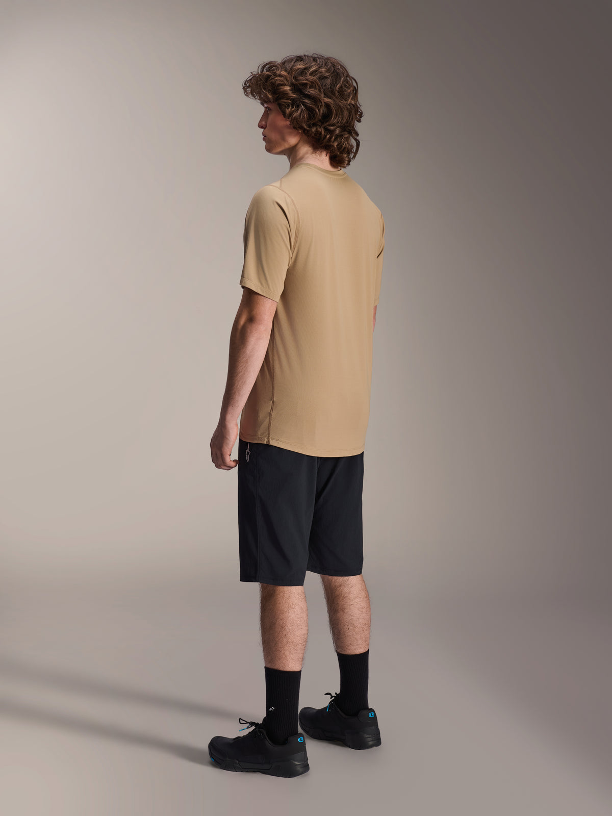Short Alpinestars A-Dura Liner en noir et maillot A-Dura SS en beige, portés par un mannequin homme de profil, associés à des chaussettes noires et des chaussures de cyclisme, vêtements lifestyle de VTT.