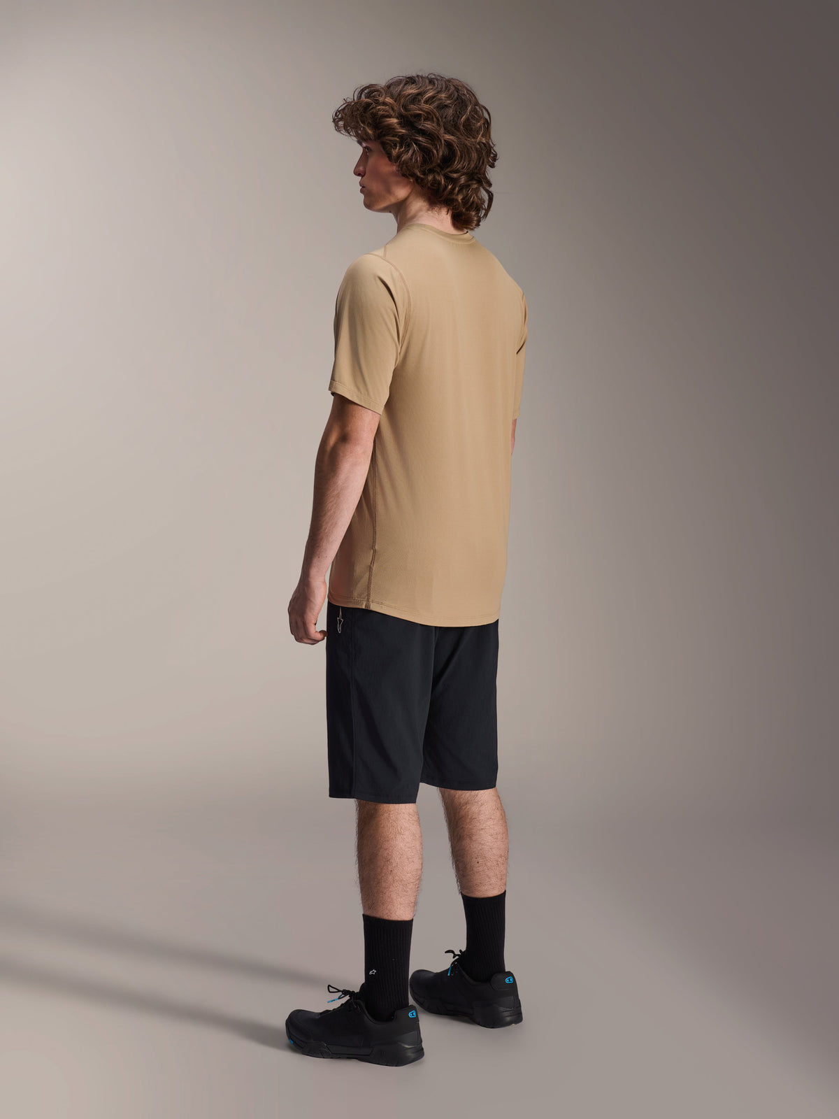 Maillot à manches courtes Alpinestars A-Dura Astar, marron clair, porté avec un short noir et des chaussettes noires, tissu jacquard évacuant l'humidité, vêtement de performance décontracté pour le VTT