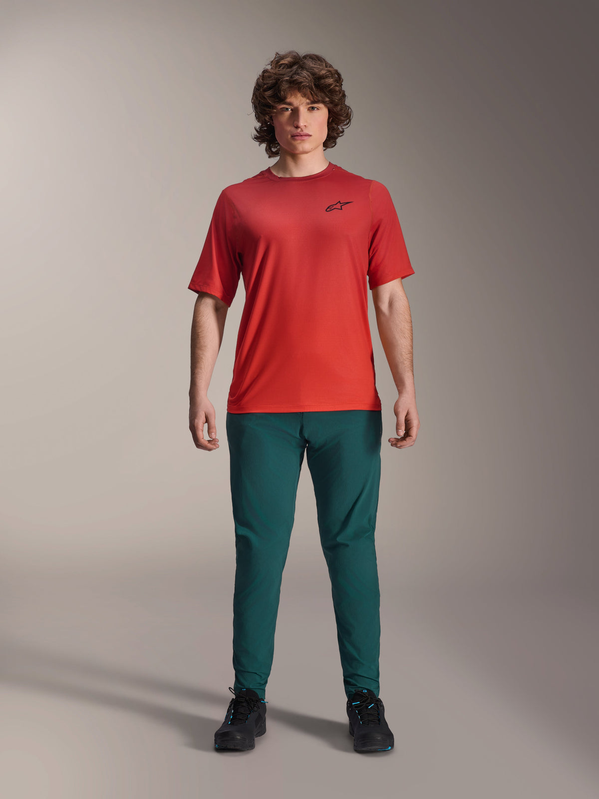 Alpinestars A-Dura Rise Short Sleeve Jersey, Spicy Orange, worn with dark green pants and black footwear, featuring a black Astars logo on the chest, casual performance mountain bike apparel for off-road riding