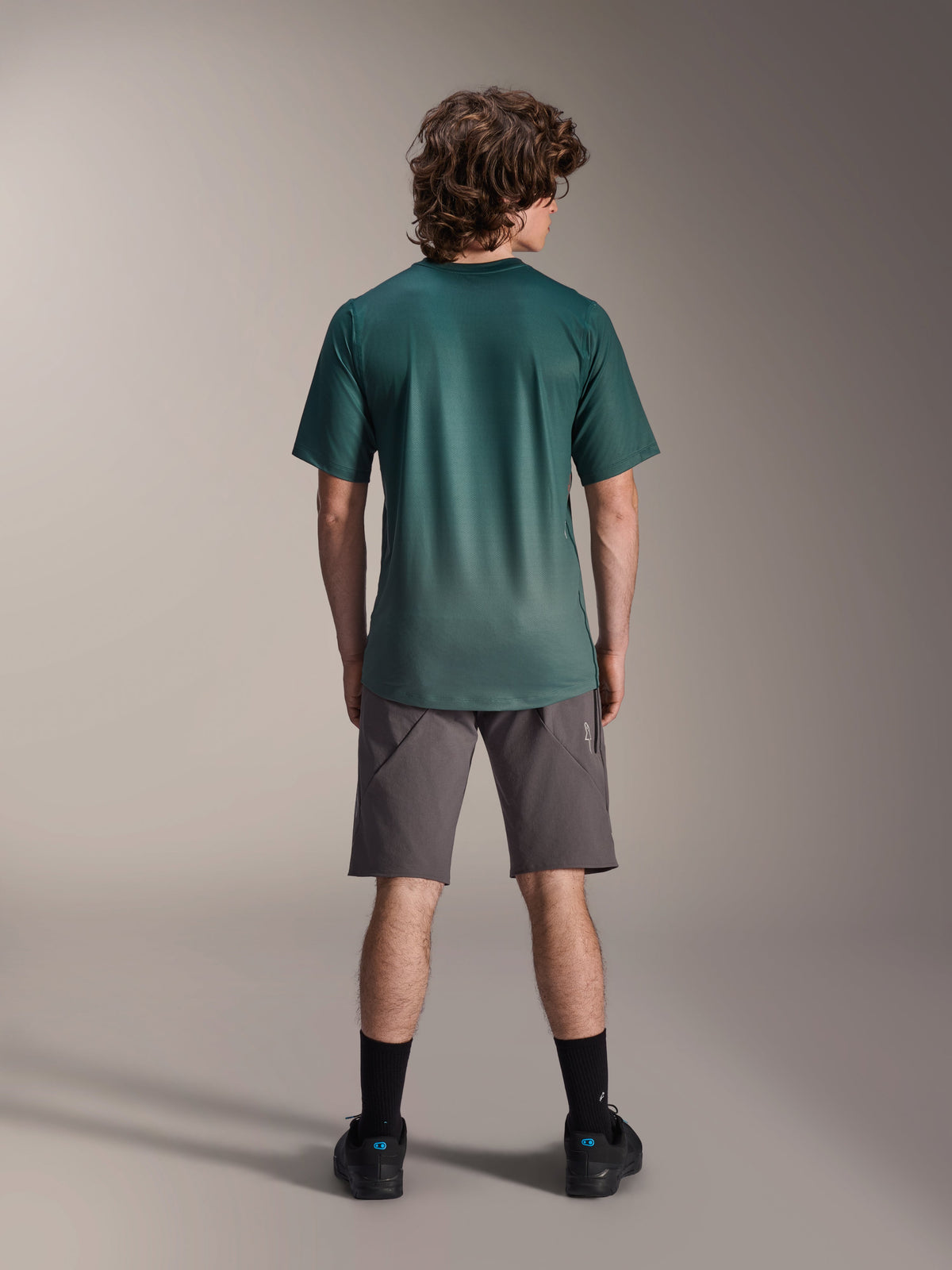 Alpinestars A-Dura Rise Jersey - Short Sleeve, Silver Pine Green, back view of a male model wearing the jersey with grey shorts and black socks, featuring a longer drop tail and regular fit for mountain biking